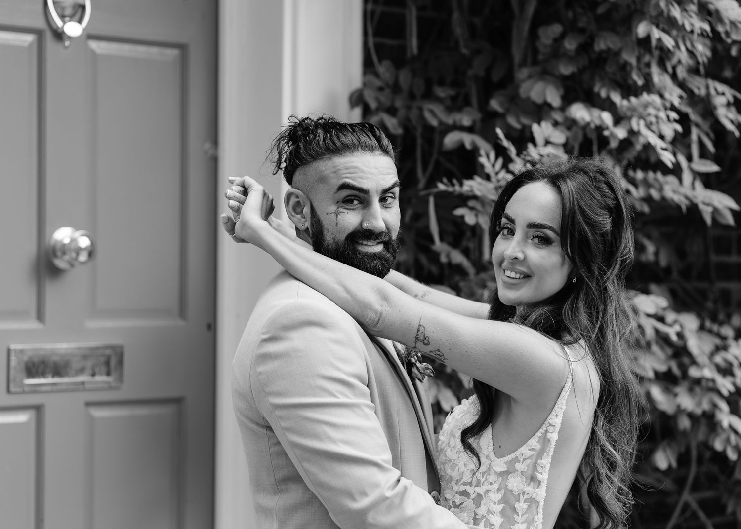 A happy couple in formal wedding attire share a joyful moment together outdoors in black and white photography.