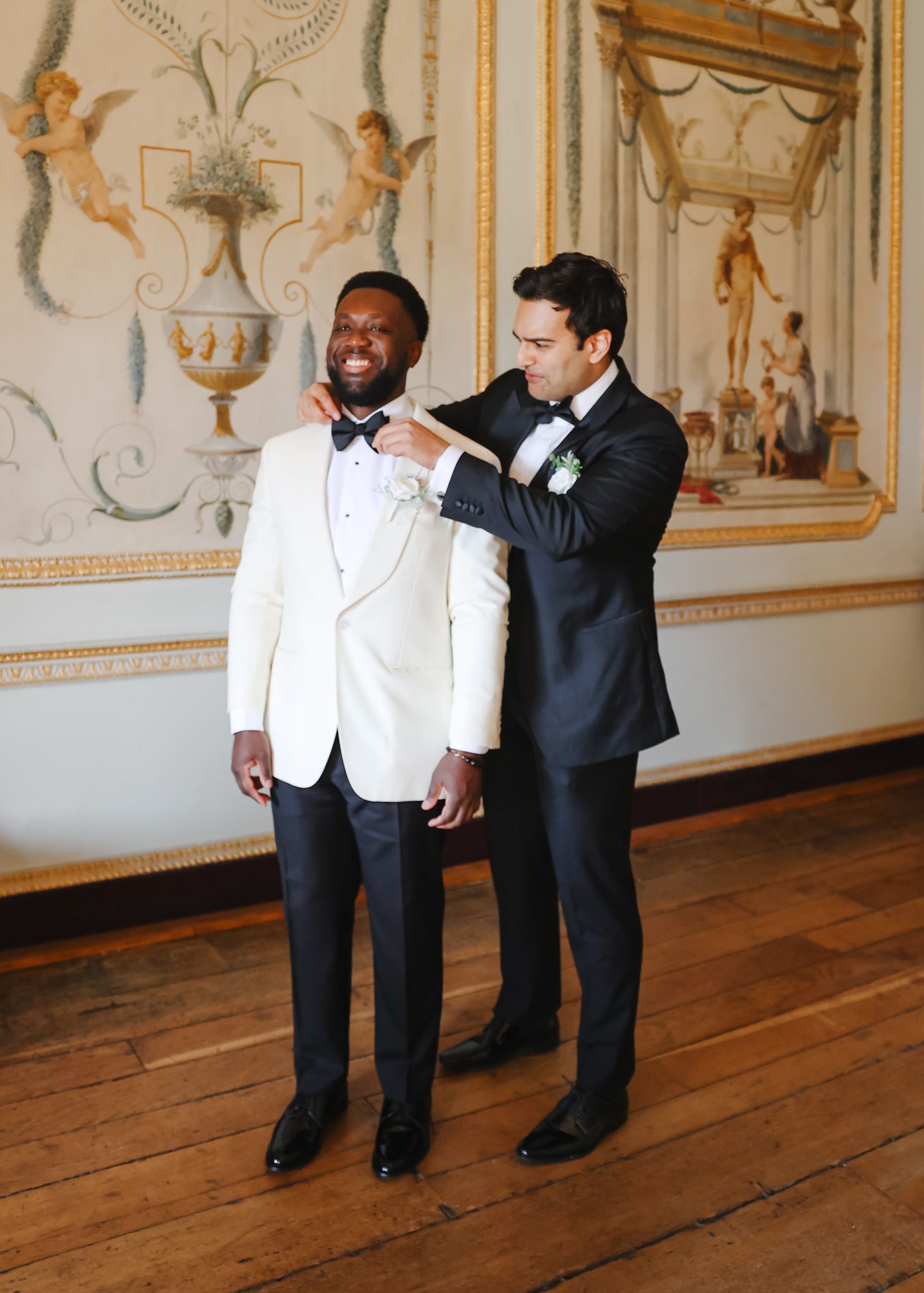 Two performers in black and white attire dance together in an ornate room with gilded walls and wooden floors.