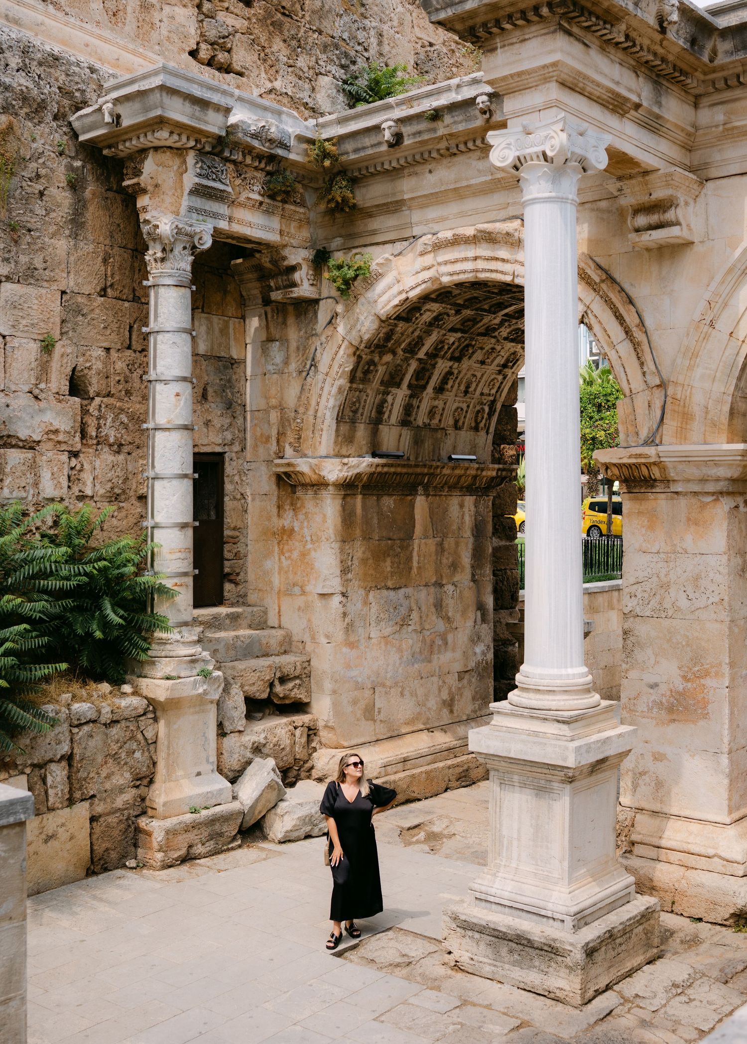Woman in black dress standing before Hadrian's Gate, ancient Roman triumphal arch in Antalya, Turkey.