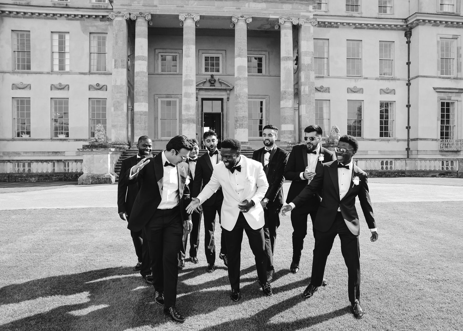 Wedding party walks and laughs together in black and white photo outside classic architecture.