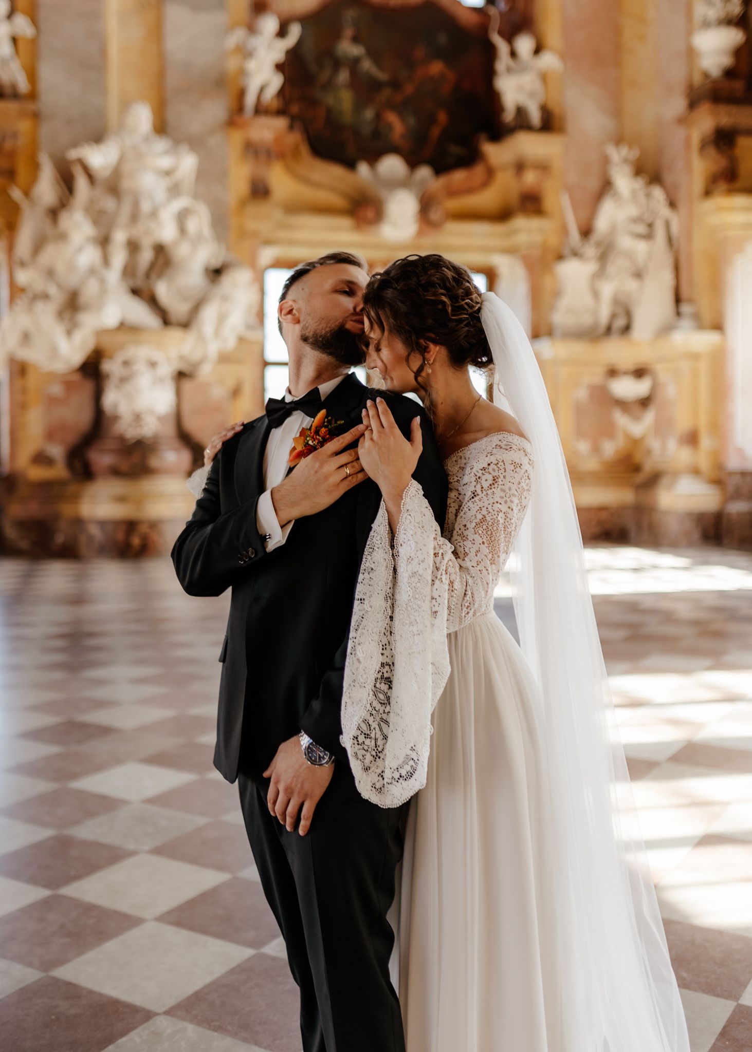 A romantic wedding couple shares tender kisses in a grand ballroom with checkerboard floors and ornate decor.