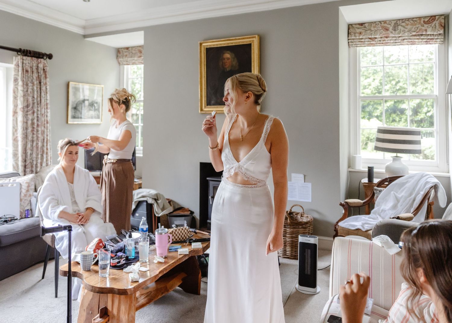 Bride in white gown getting ready with bridesmaids in elegant room, makeup and hair styling before wedding ceremony.