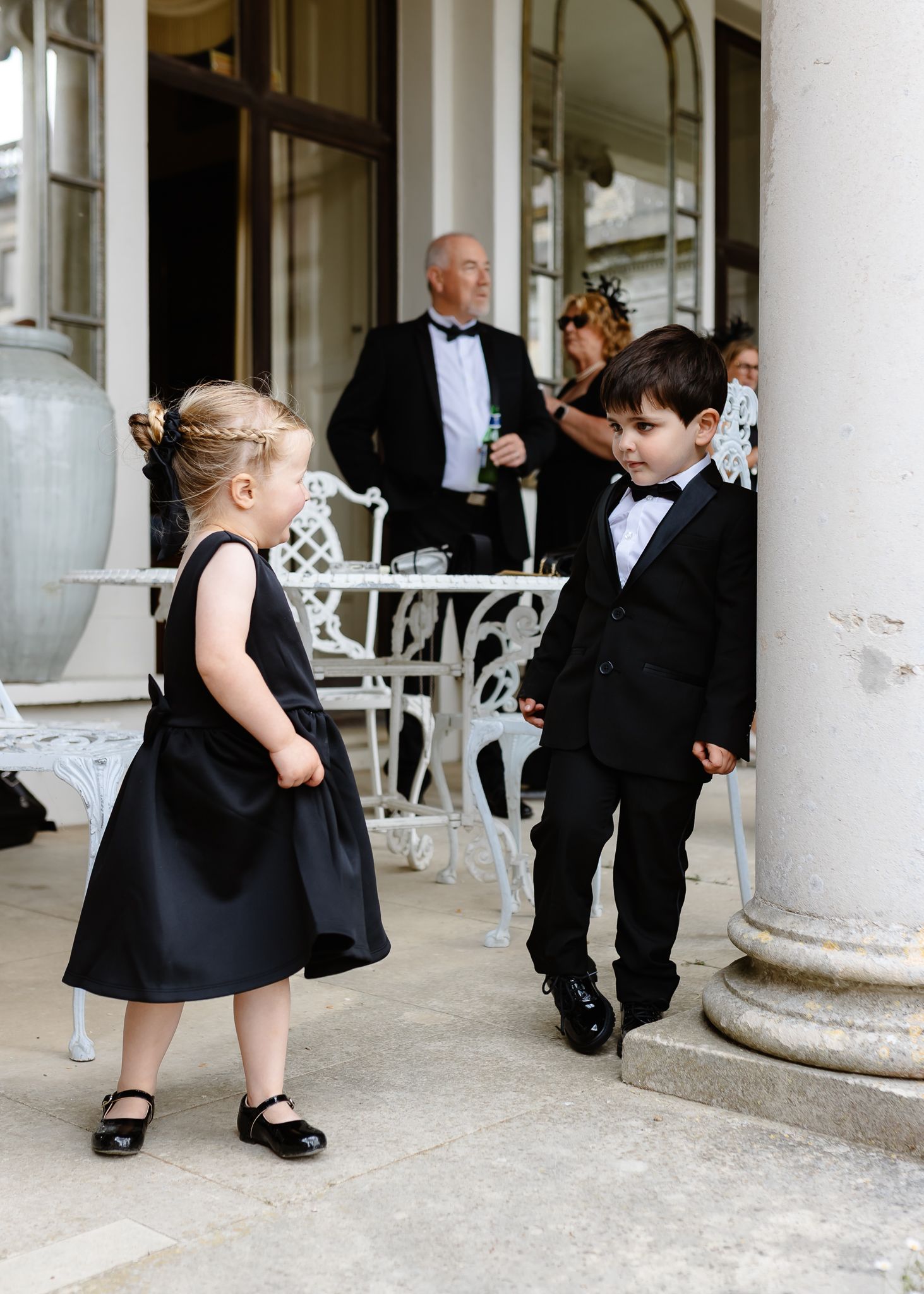 Wedding party in formal black attire gathered around white columns on a porch.