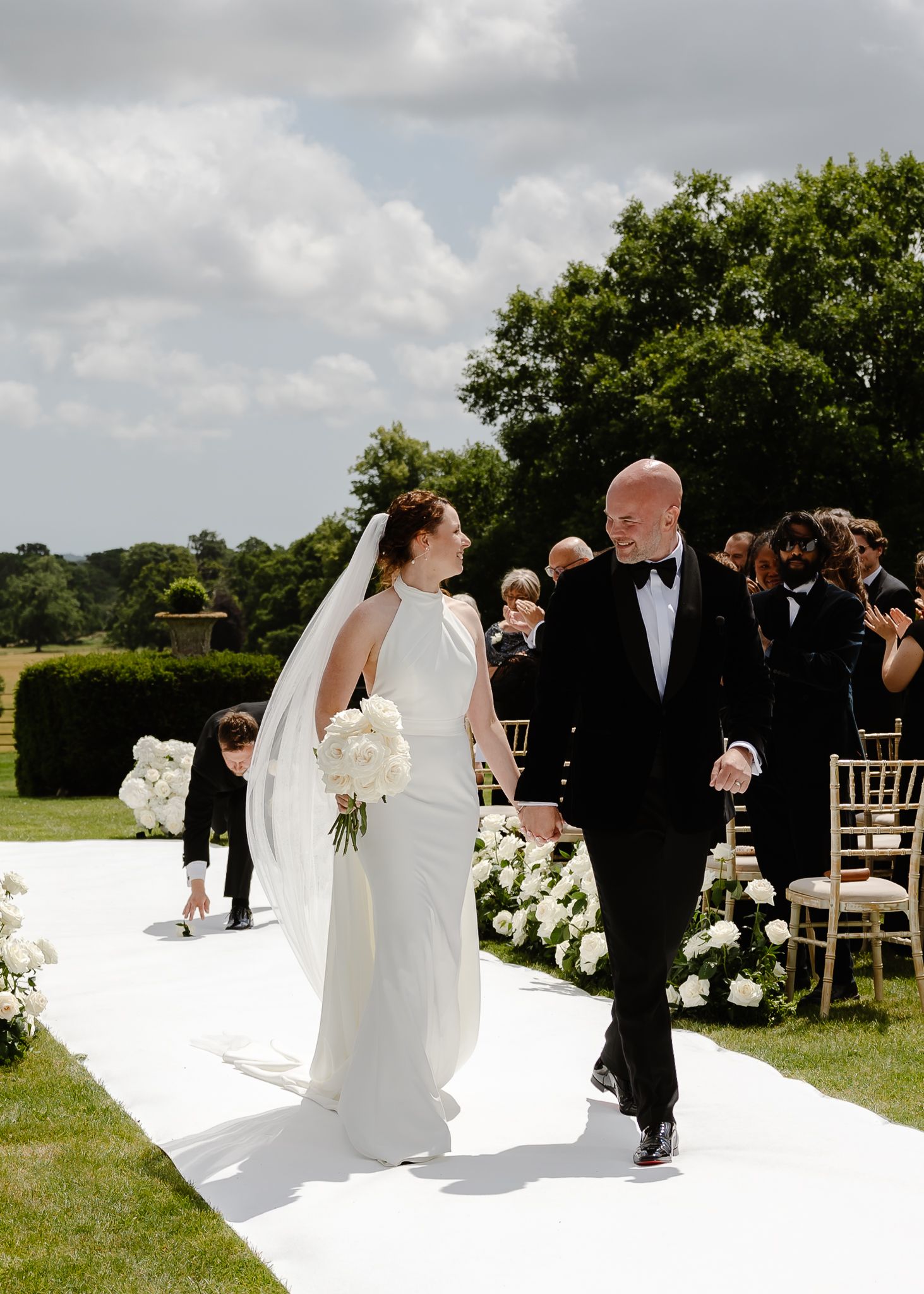 A wedding couple shares an intimate moment during their outdoor ceremony on a grassy field with elegant white decor.