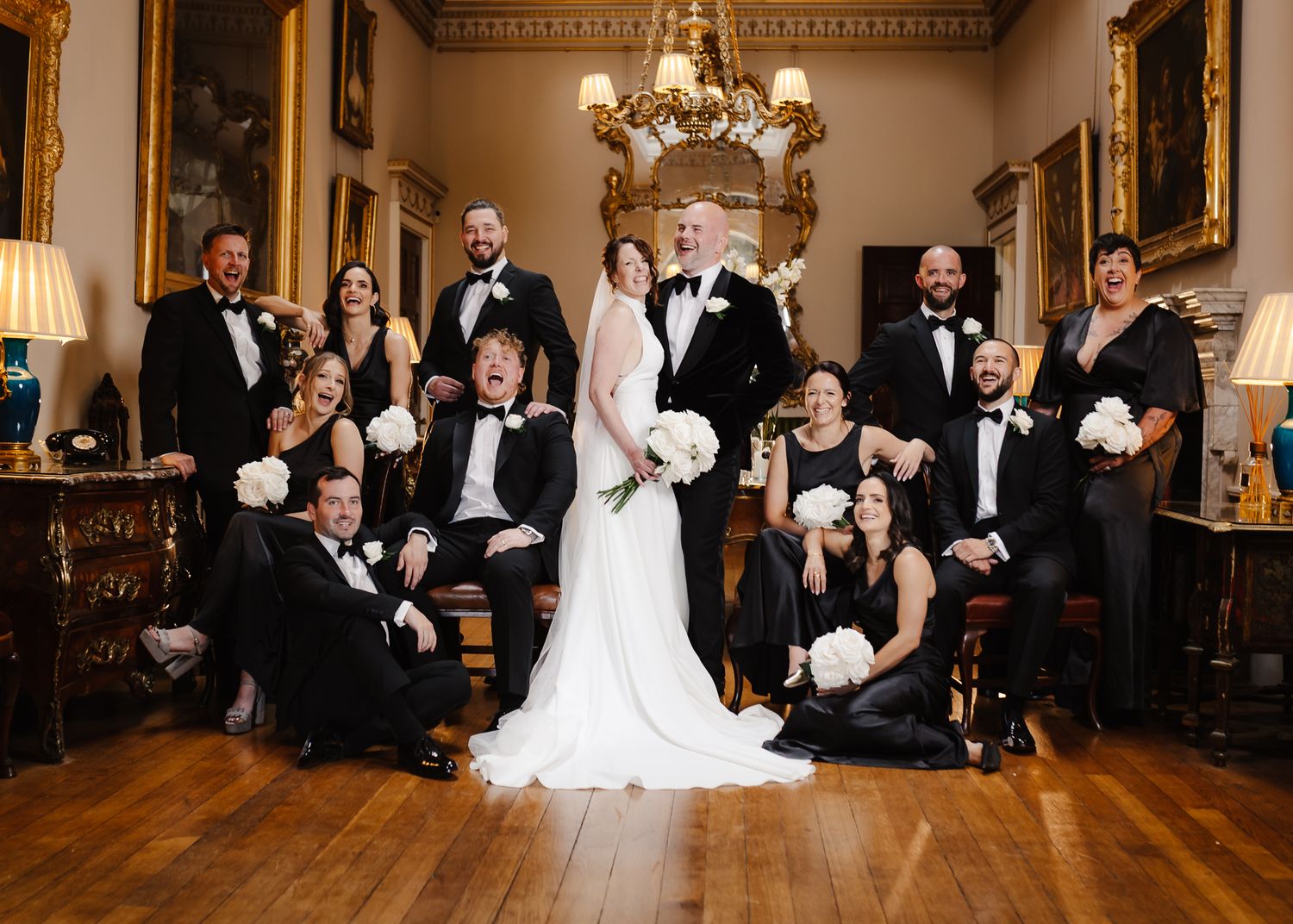 Formal wedding party poses in an ornate ballroom with elegant decor and lighting.