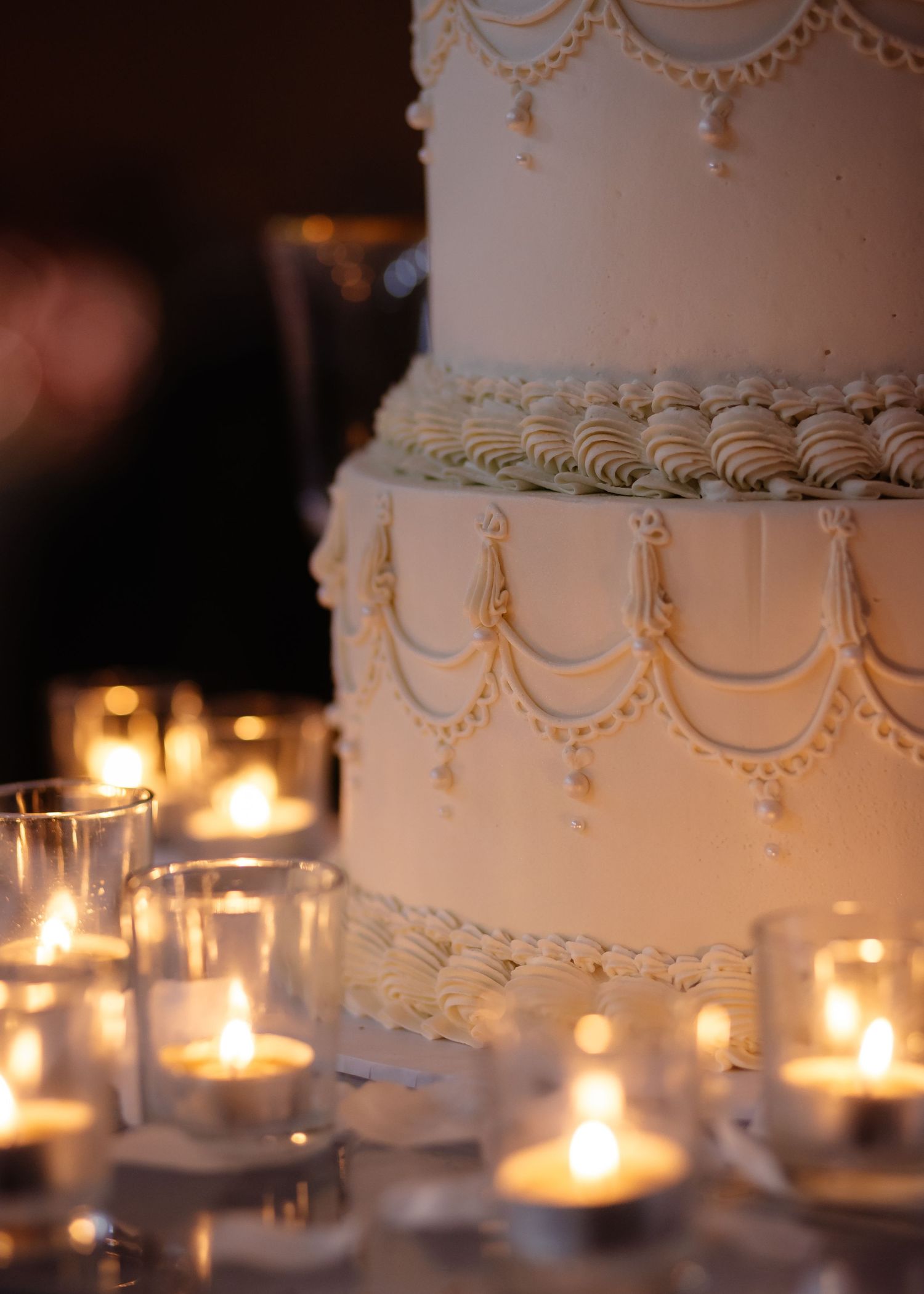Elegant multi-tiered white wedding cake with swag frosting details, surrounded by glowing candlelight at a romantic reception.