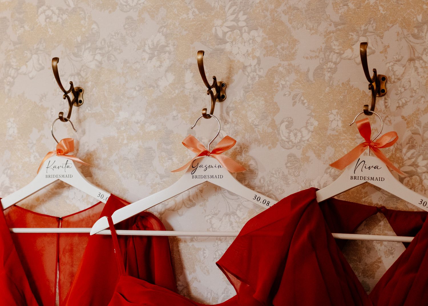 Red bridesmaid dresses hanging on white hangers against a textured beige wall.