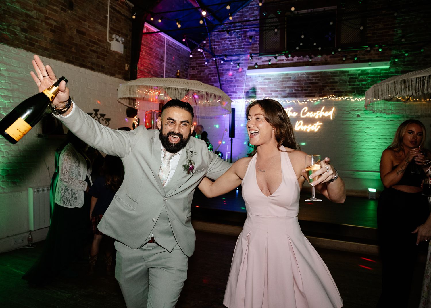 Wedding party dancing and celebrating in a venue with colorful mood lighting.