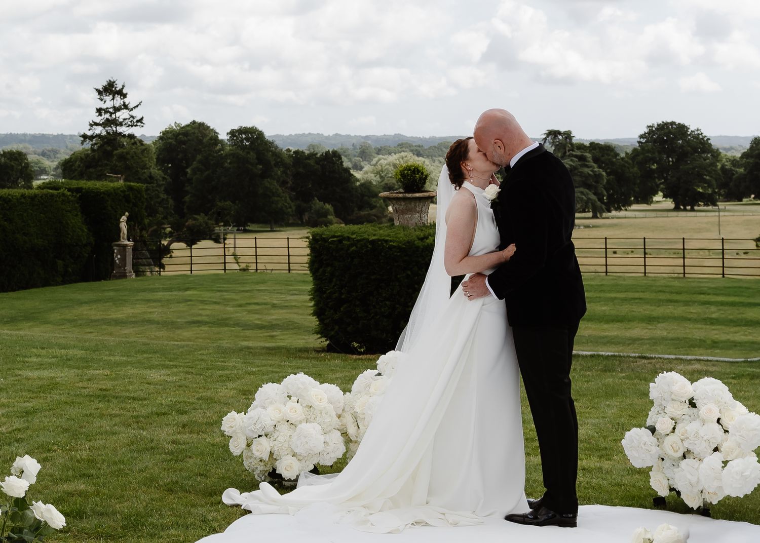 Elegant wedding ceremony on a manicured lawn with white floral arrangements.
