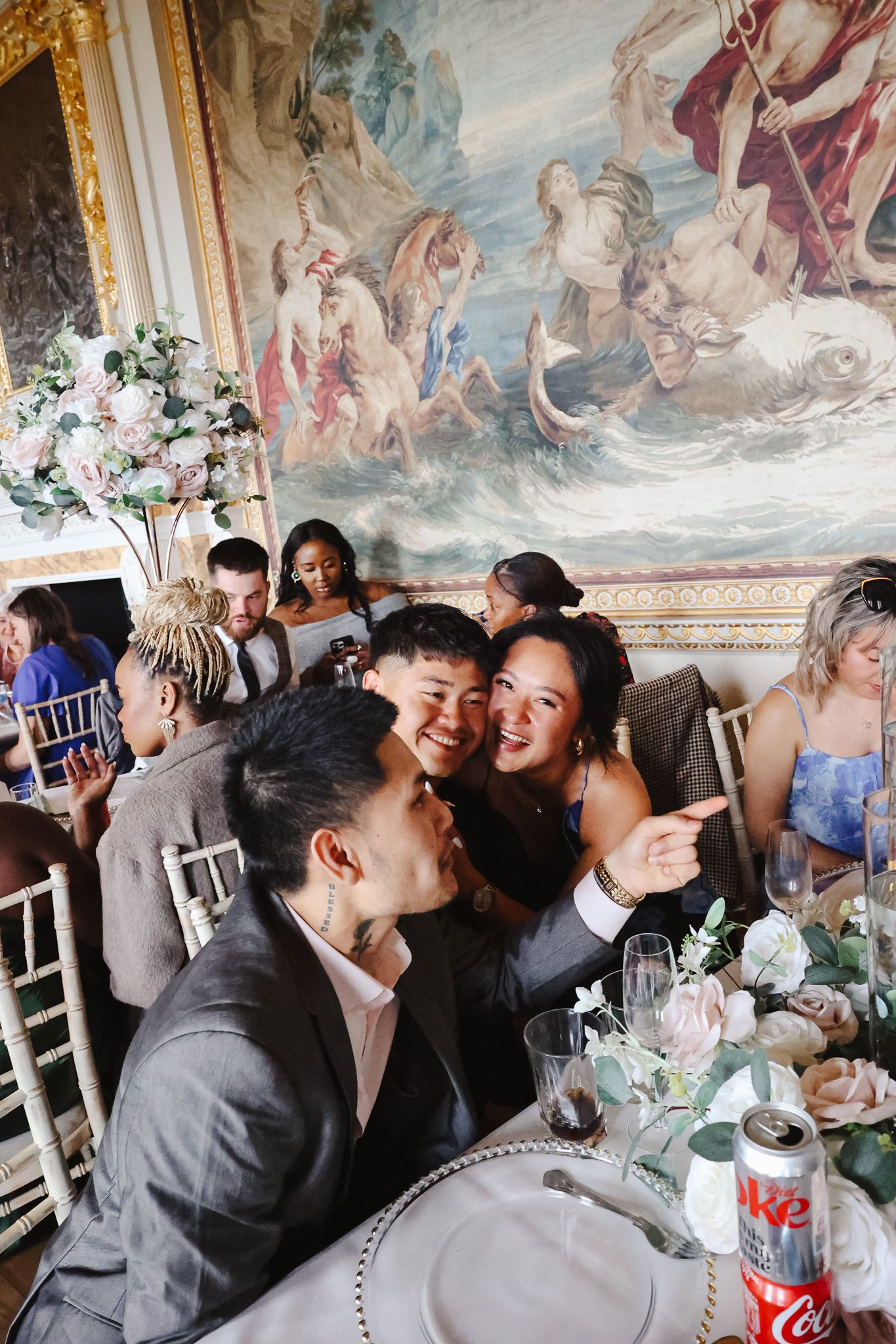 A group of guests enjoying a celebration in an elegant room with ornate ceiling murals and white chairs.