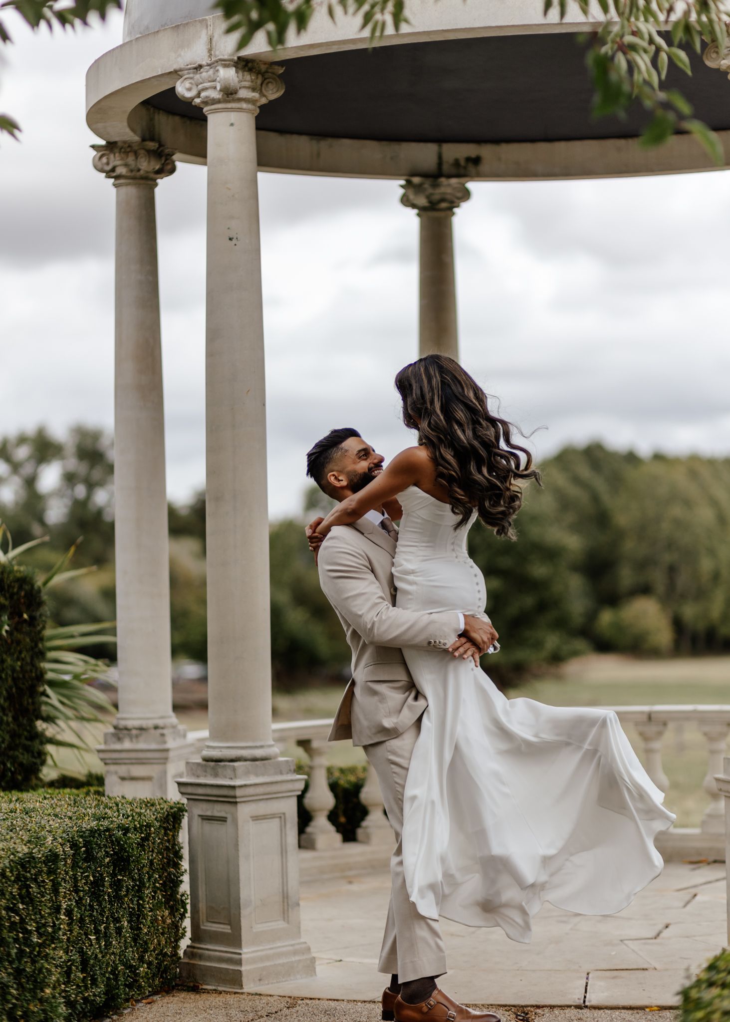 A romantic couple dances gracefully under a white gazebo surrounded by lush greenery during their wedding celebration.