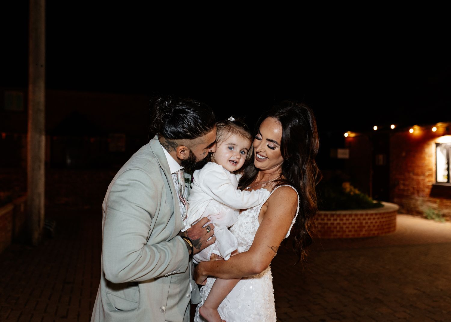 A couple in formal wedding attire sharing intimate moments during an outdoor nighttime celebration.