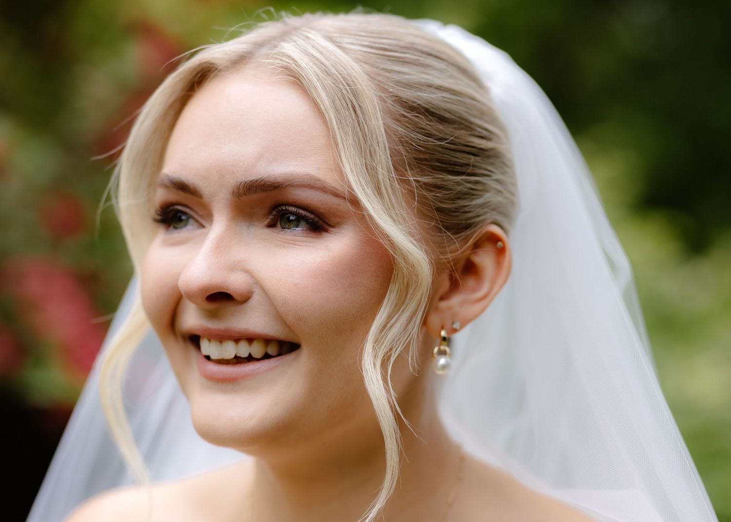 Smiling bride wearing a white veil and pearl earrings with elegant updo hairstyle on her wedding day.