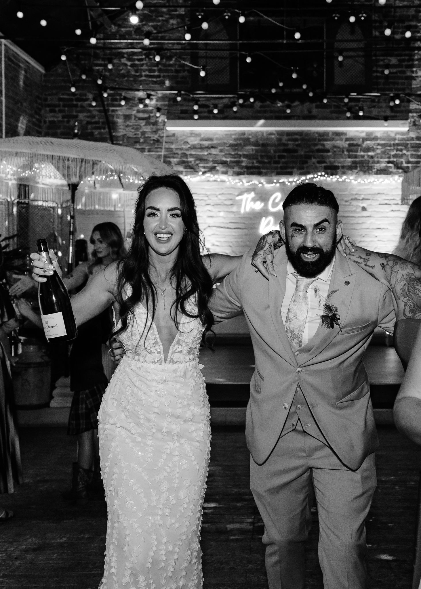 Wedding celebration with guests dancing under string lights in an industrial-style venue.