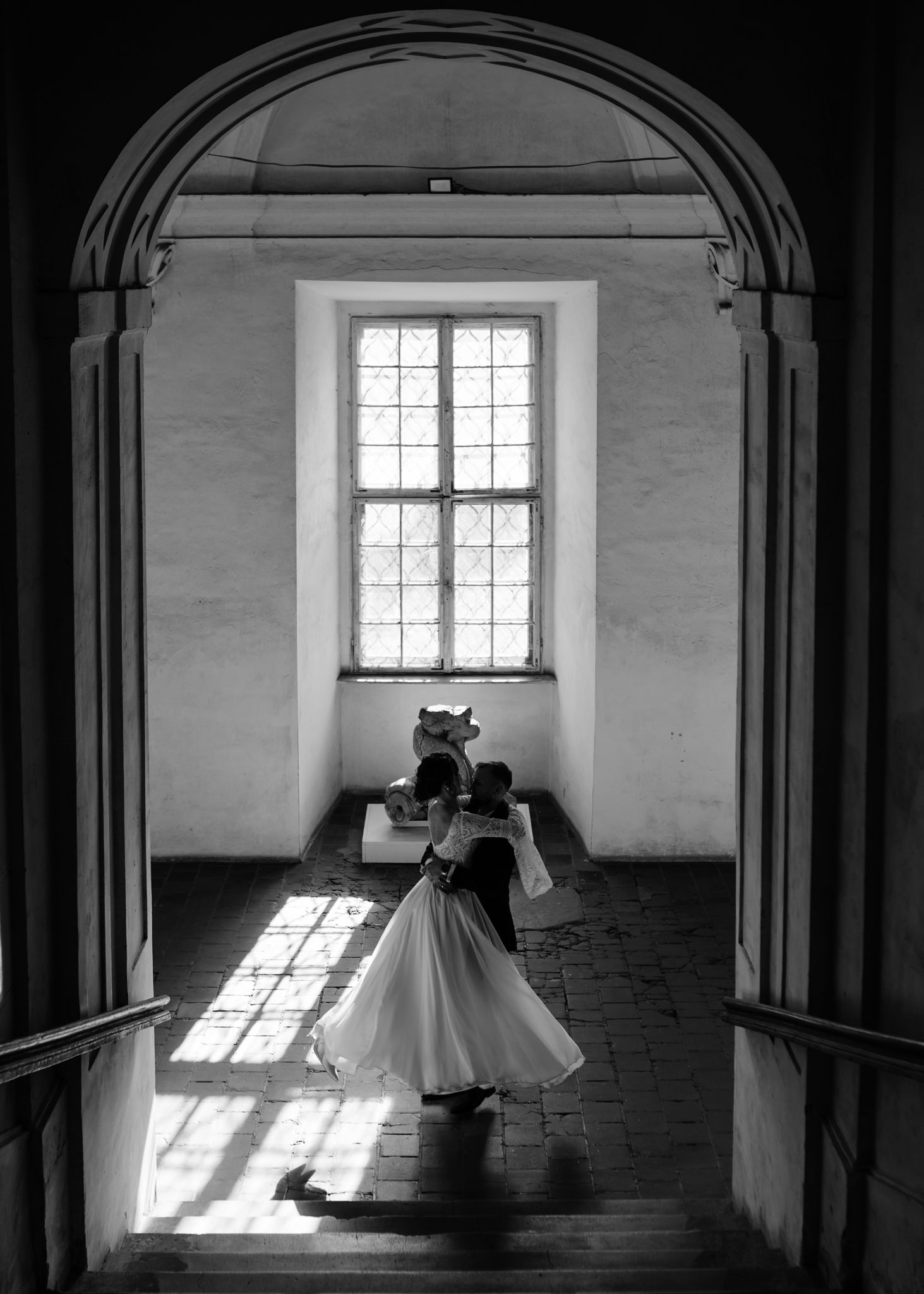 Black and white series showing wedding couple silhouetted against arched windows in historic building.