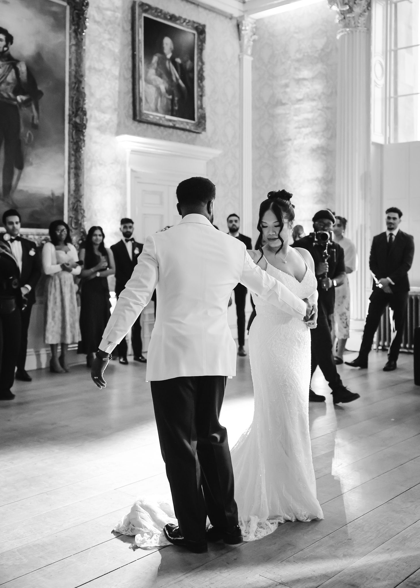 Wedding couple shares first dance in classic black and white photo inside historic ballroom.