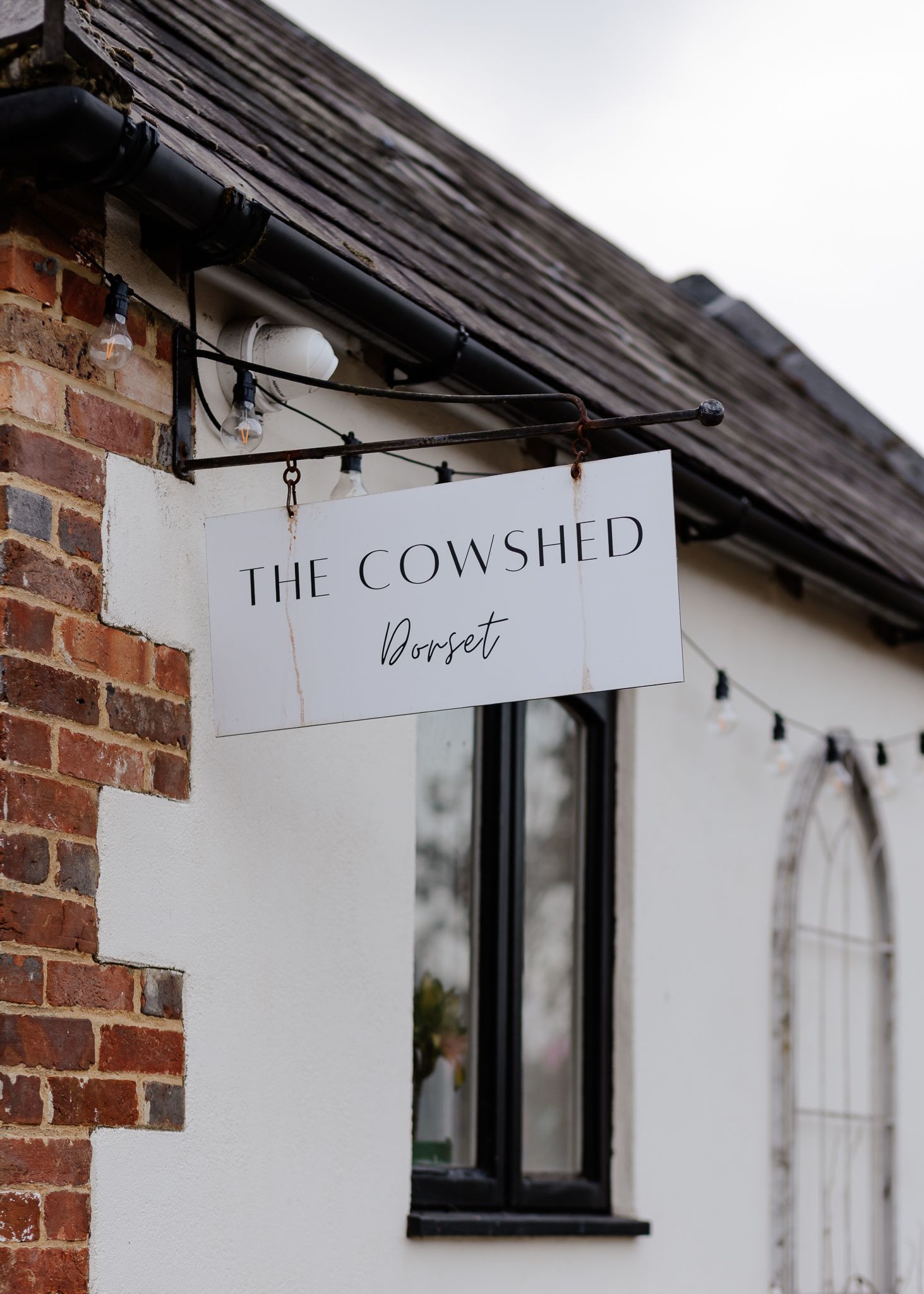 A rustic sign reading 'The Cowshed' hangs from a wooden beam against exposed brick walls.