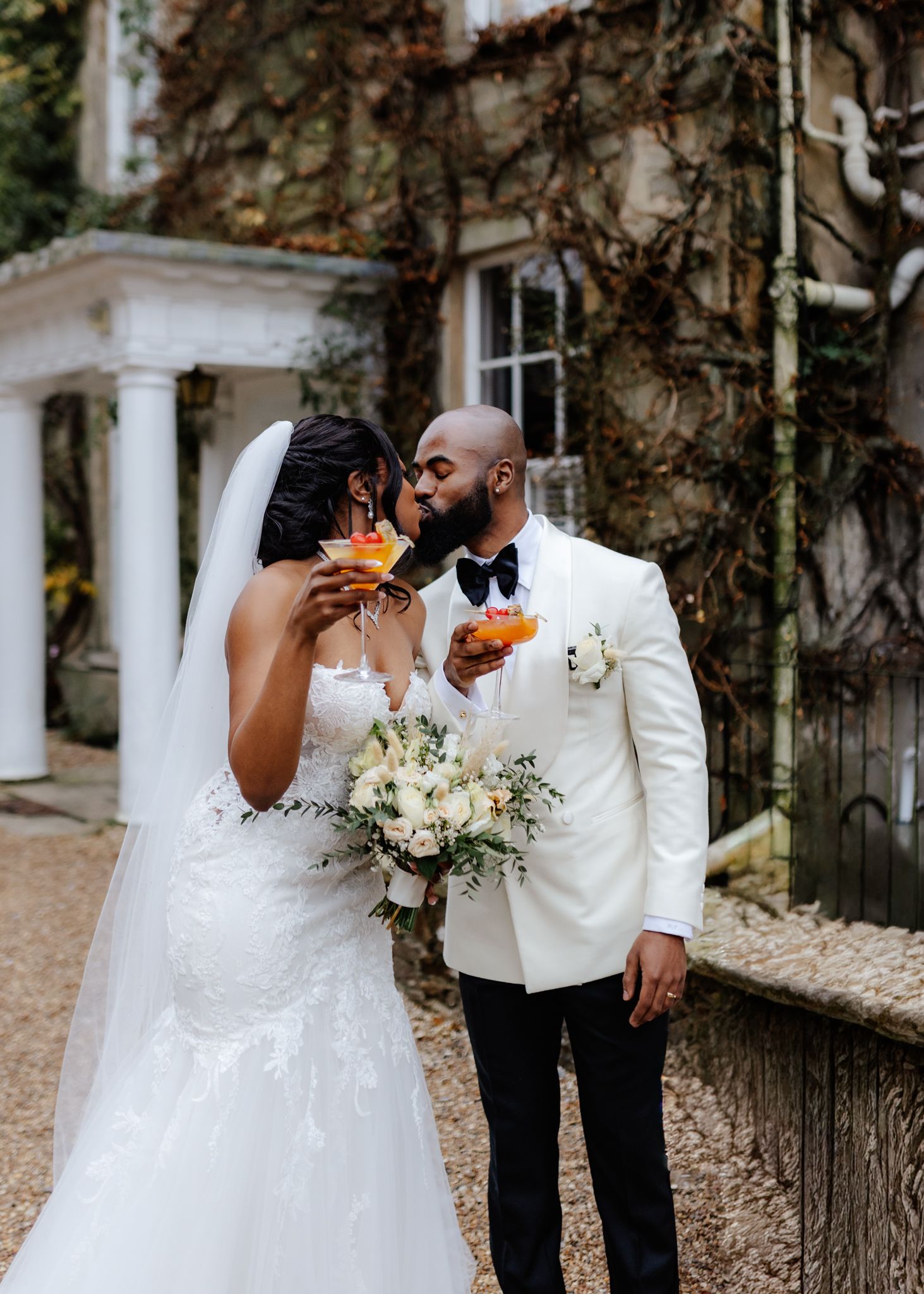 A romantic wedding couple shares intimate moments in a garden setting with white columns and natural scenery.