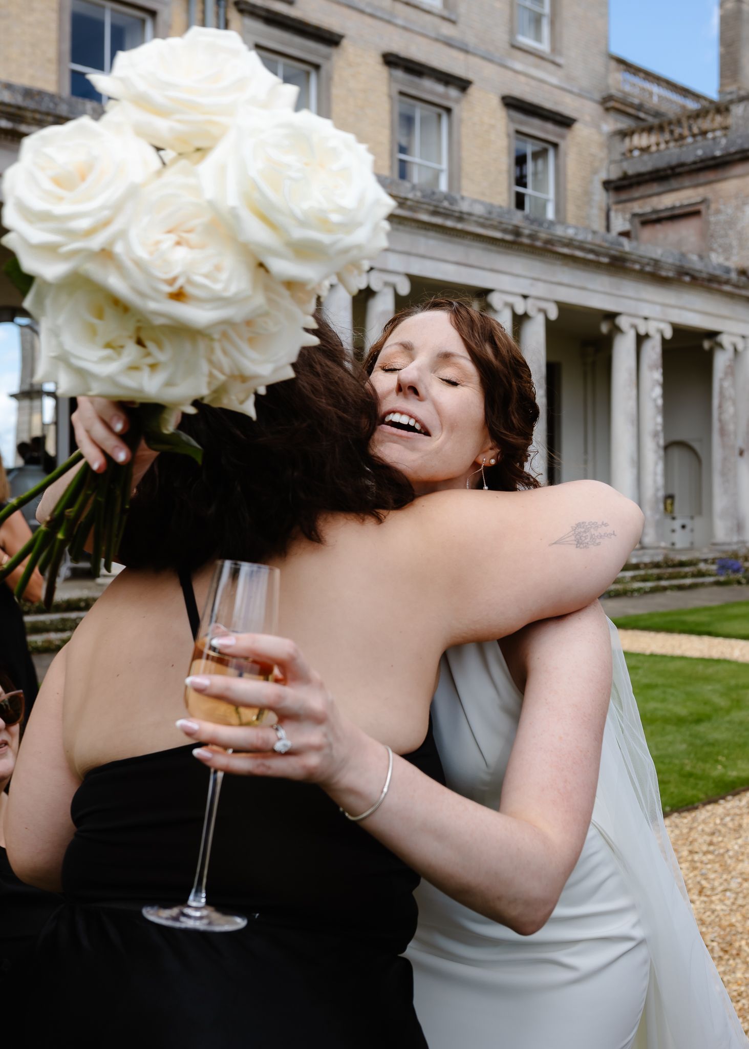 Two people share an emotional embrace with white roses and champagne at an elegant venue.