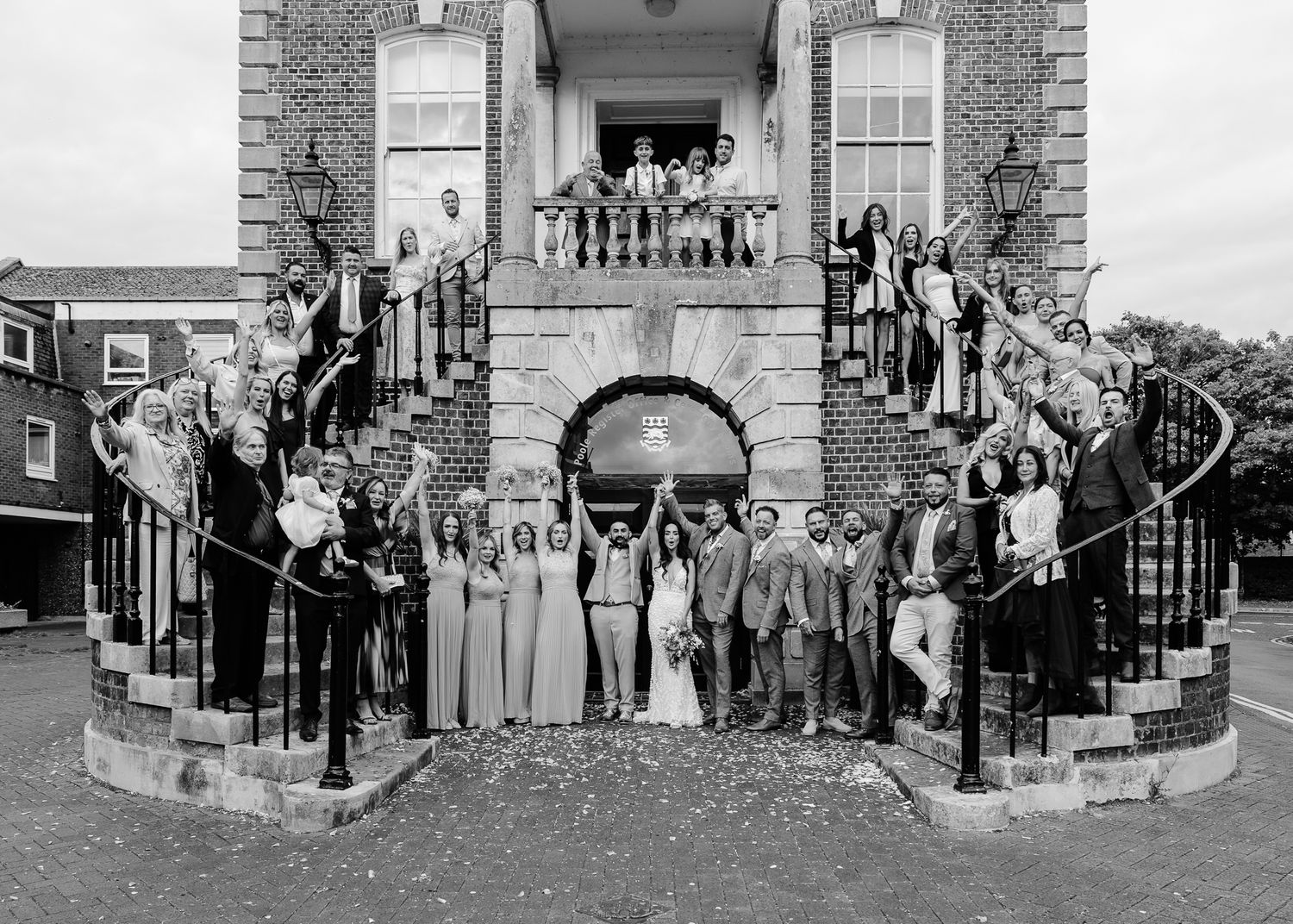 A black and white panoramic photograph showing a group of people gathered outside a historic brick building.
