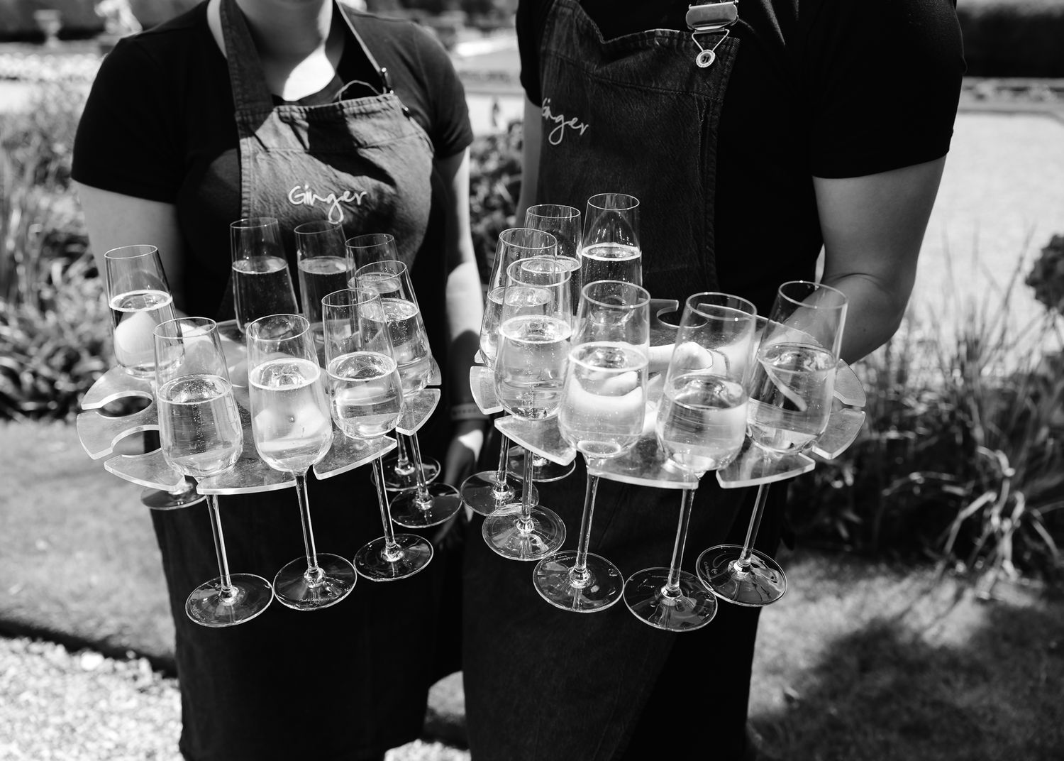 Servers hold trays of champagne glasses at an elegant outdoor event.