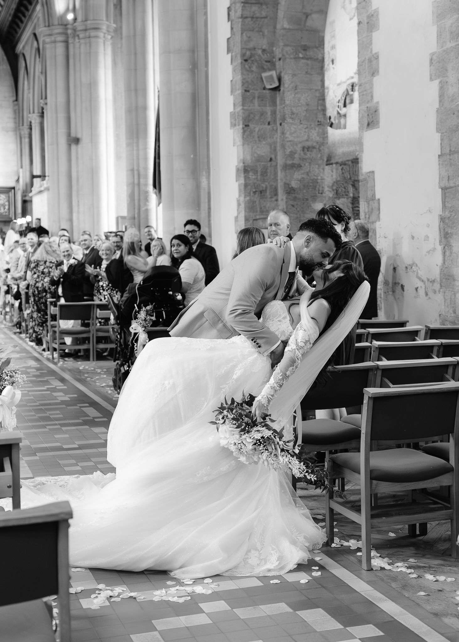 A bride in a flowing white dress lies gracefully across church pews during a wedding ceremony.