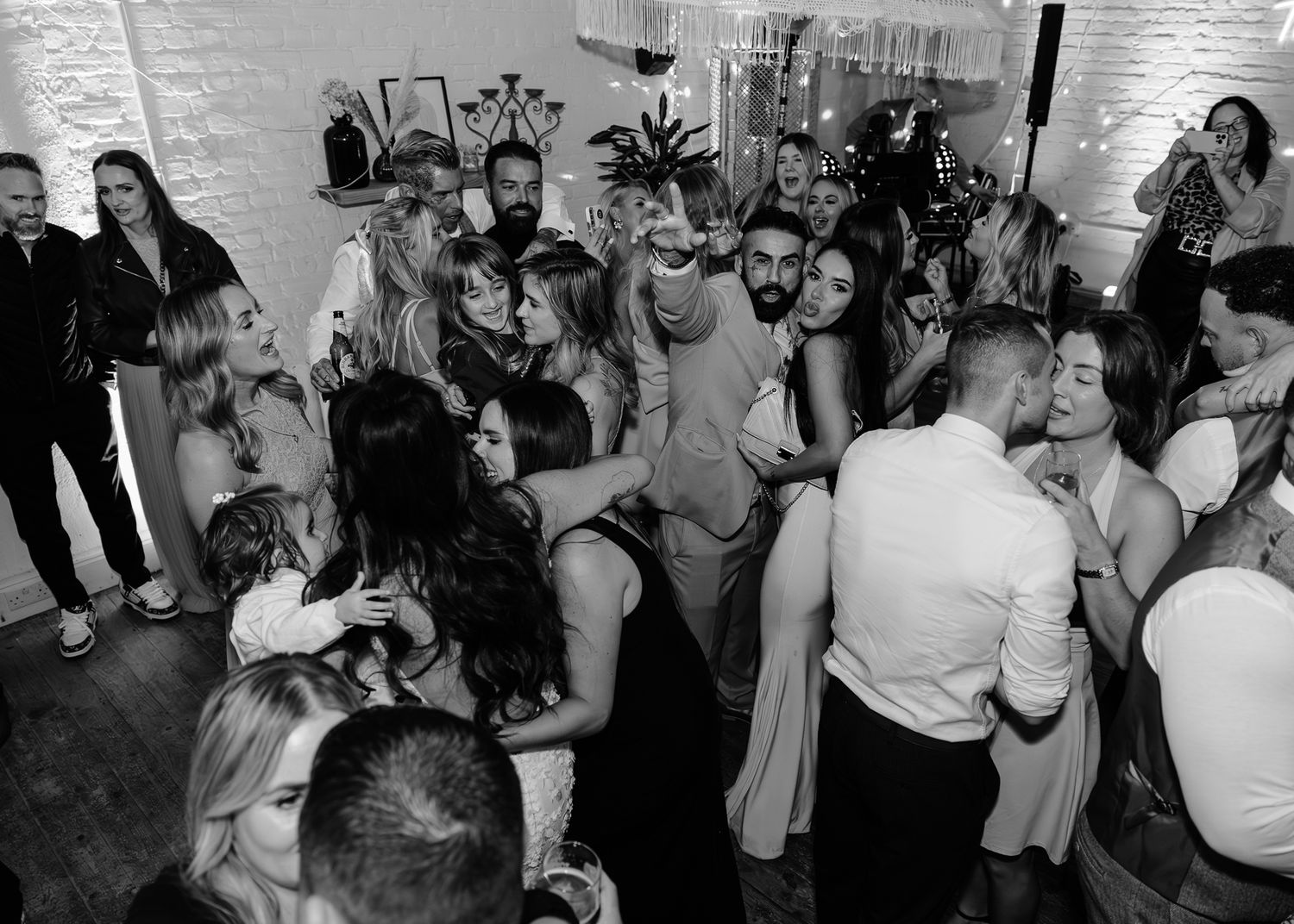 Black and white photo montage of wedding guests dancing and celebrating at a reception party.