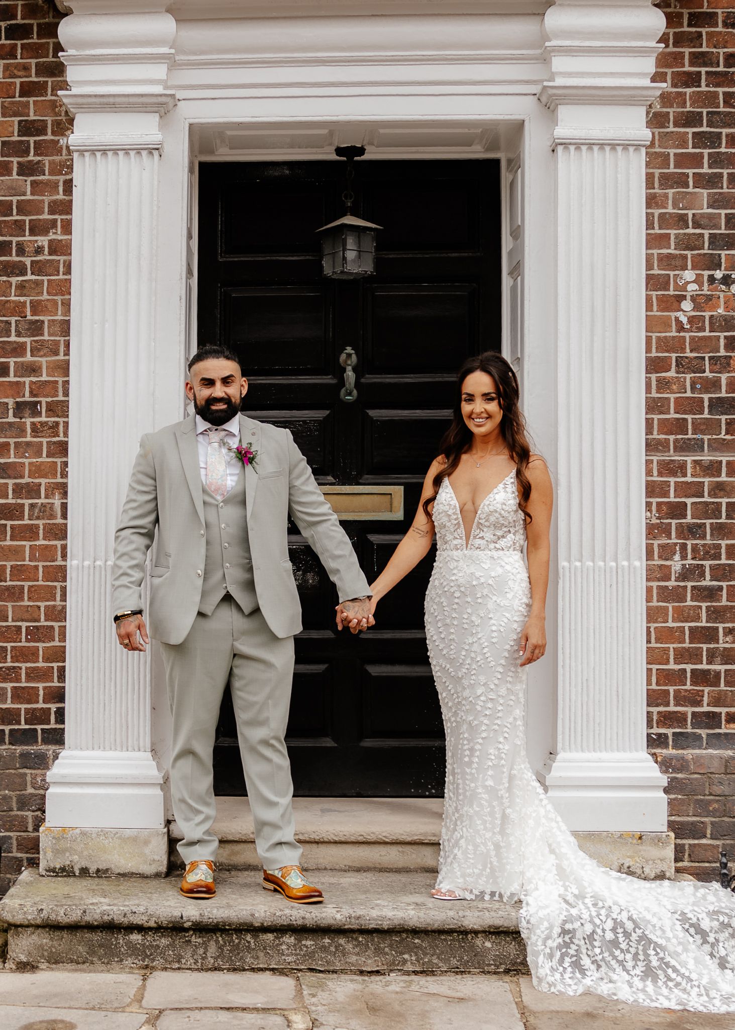 Wedding party poses creatively in doorways of historic brick building with white columns and elegant attire.