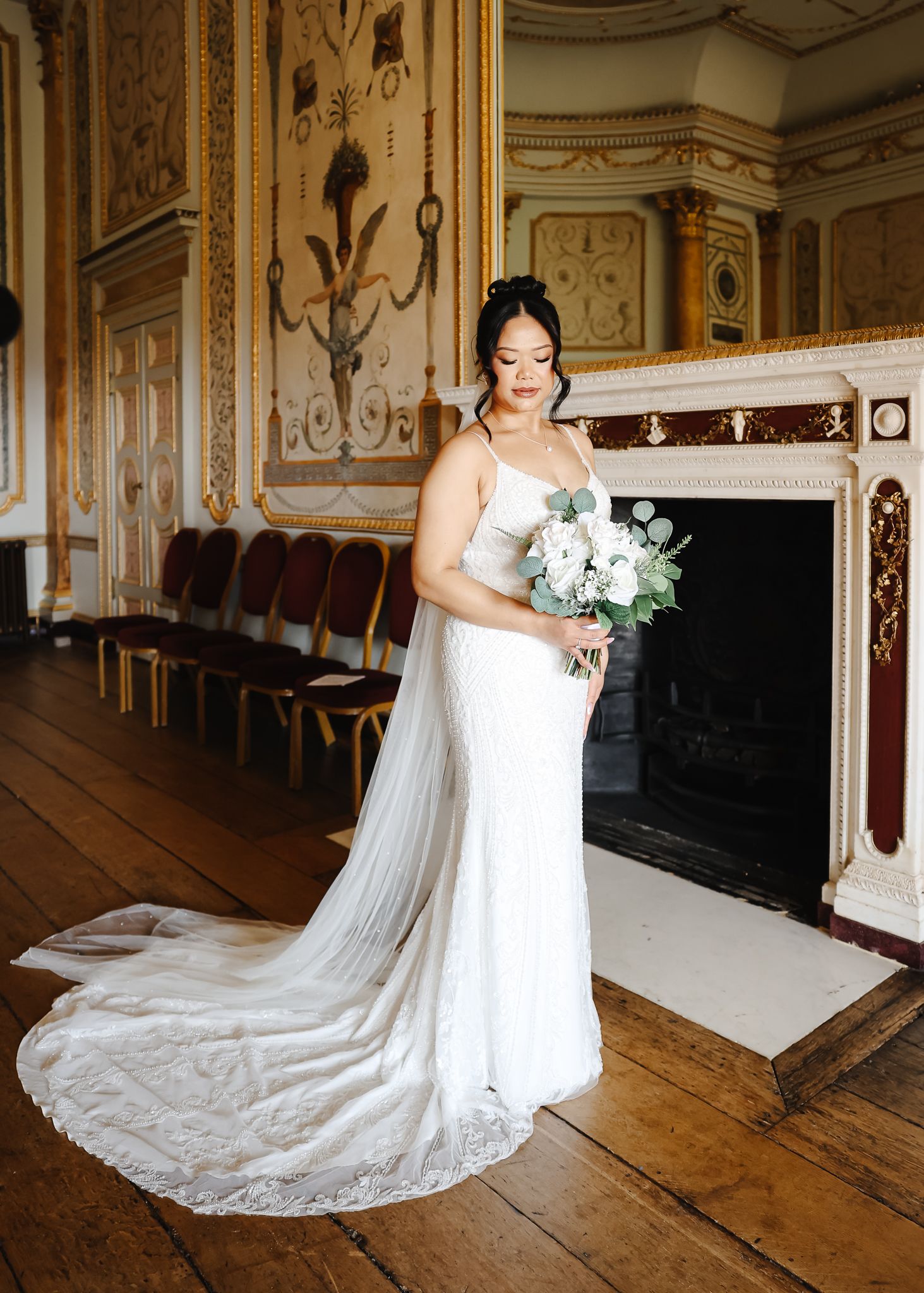 Wedding gown with delicate lace train photographed in elegant historic room with ornate wall panels.