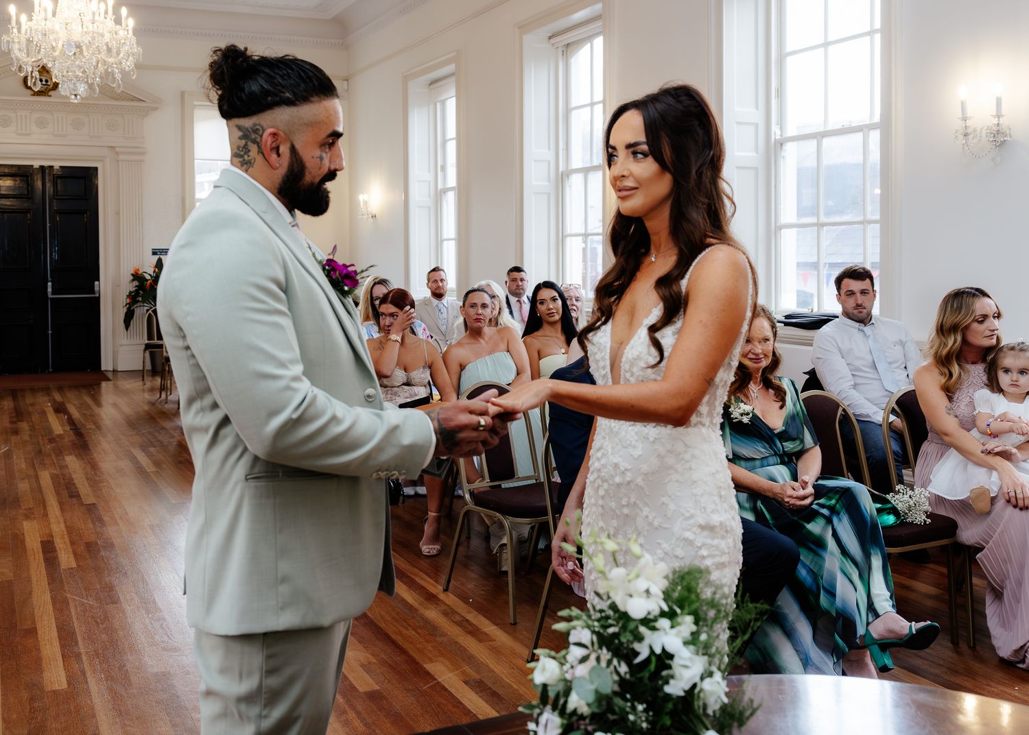 A wedding couple shares their first dance in an elegant ballroom with a crystal chandelier overhead.