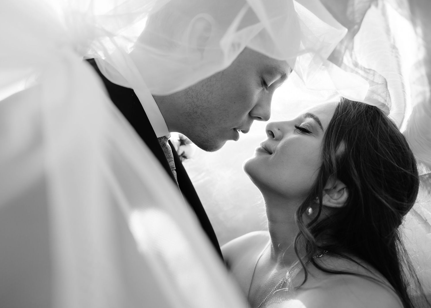 Black and white wedding photo of bride and groom sharing an intimate moment under a flowing veil.