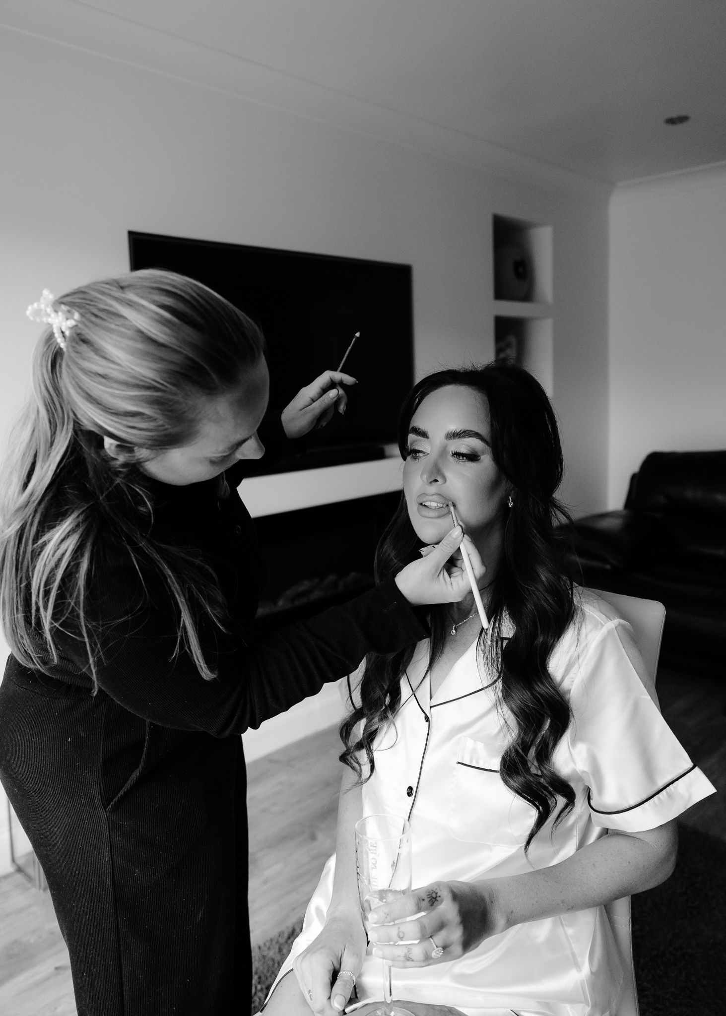 A black and white photo sequence showing someone getting their makeup professionally applied in a bright room.