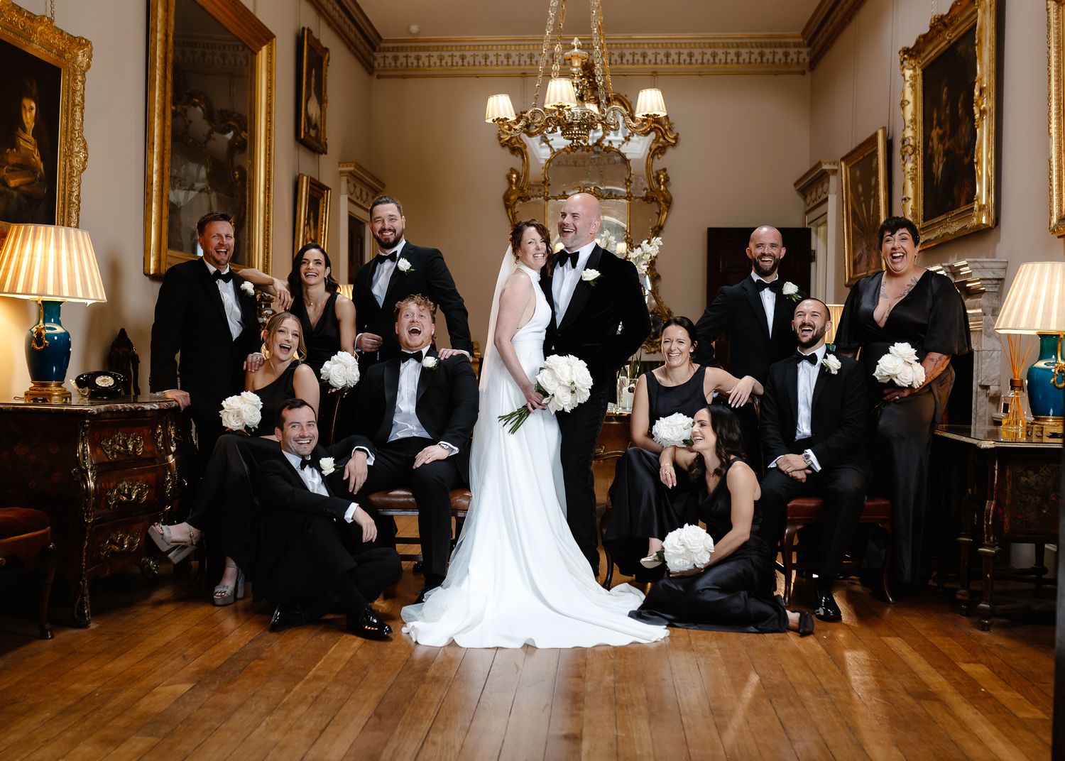 Wedding party poses together in an elegant ballroom with ornate decor and warm lighting.