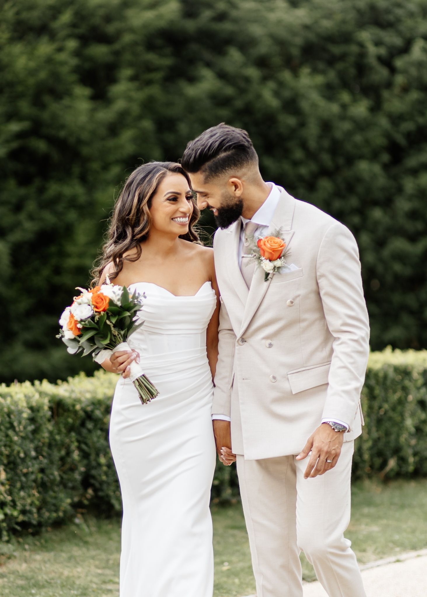 A couple in white attire share intimate moments during their wedding photoshoot in a lush garden setting.