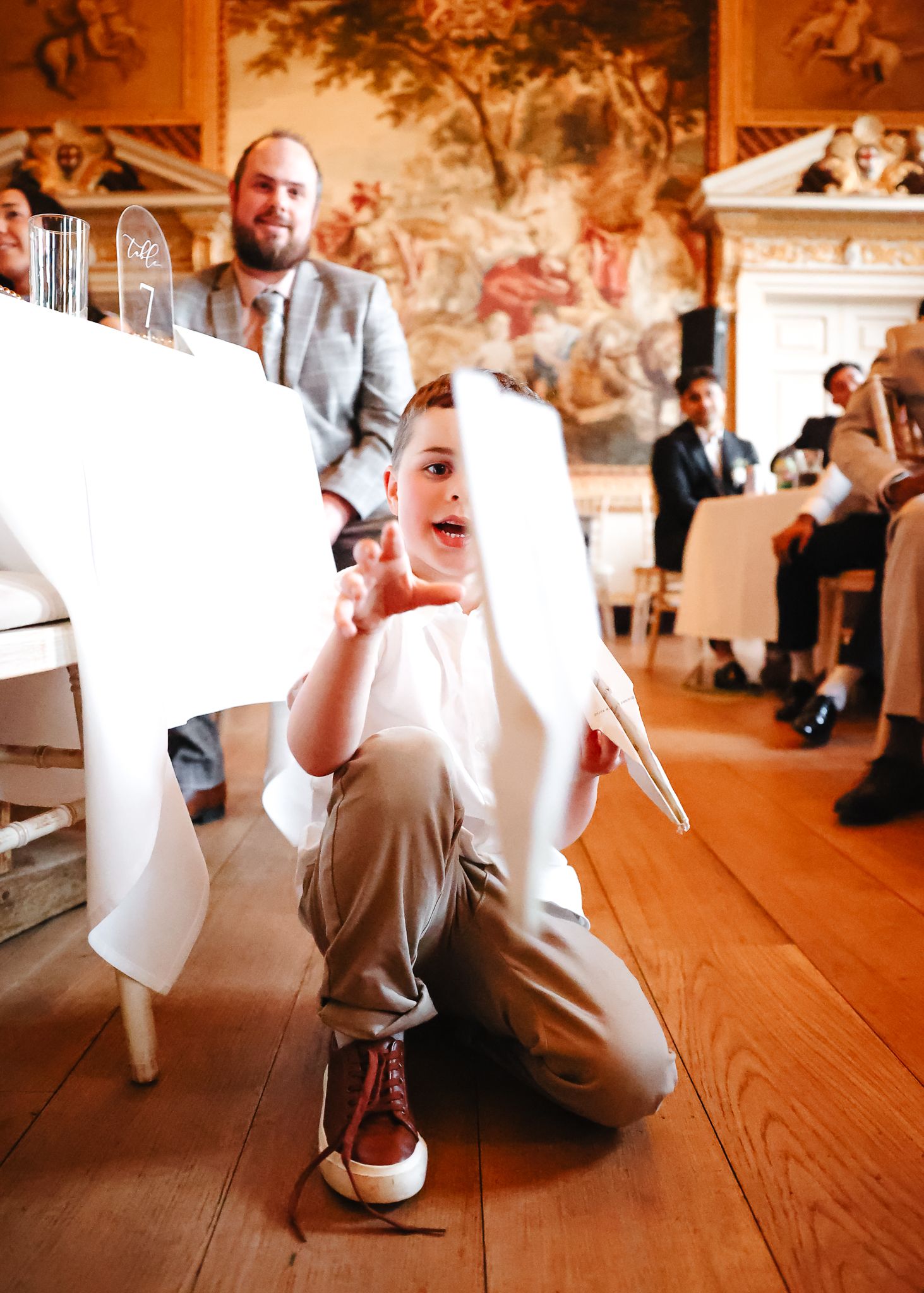 Wedding guests seated at tables in historic room with hardwood floors.
