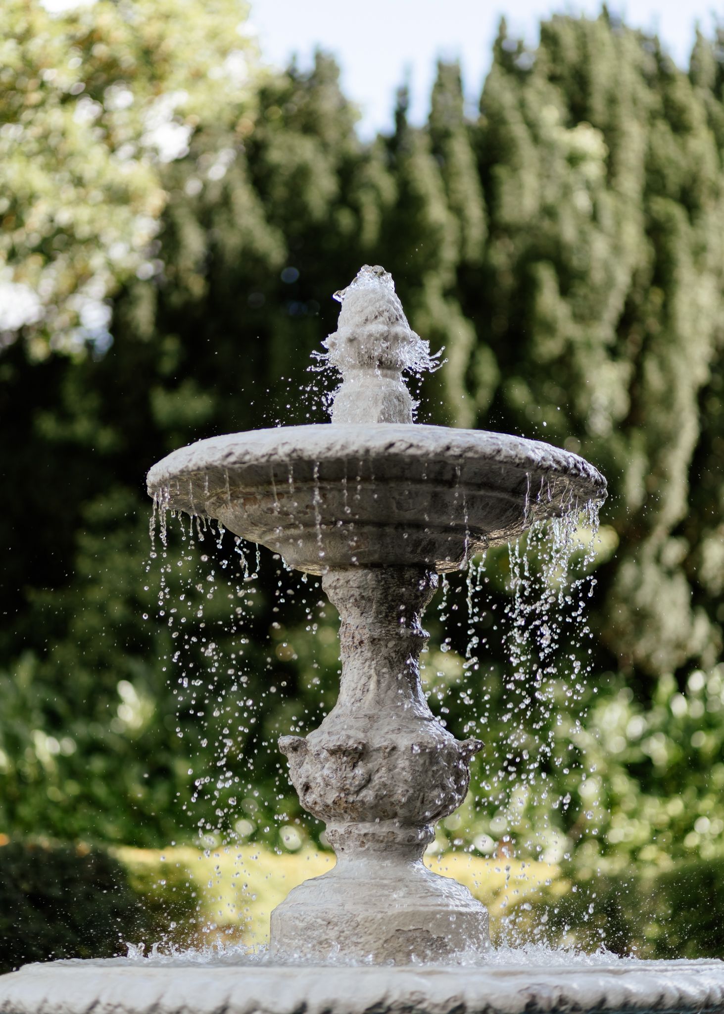 A stone garden fountain sprays water in multiple shots showing water droplets sparkling in sunlight.