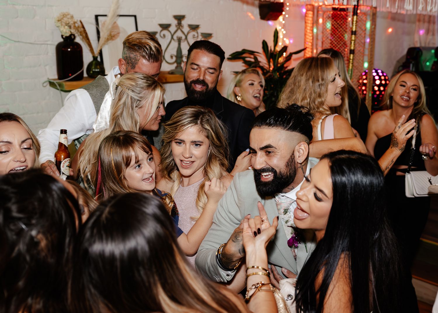 Lively wedding reception with guests dancing and celebrating in a brick-walled venue.