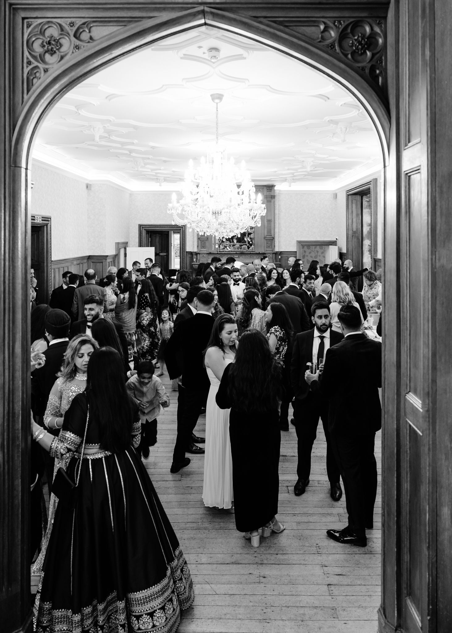 A black and white panoramic photograph shows a crowded formal event with people mingling in an ornate ballroom.