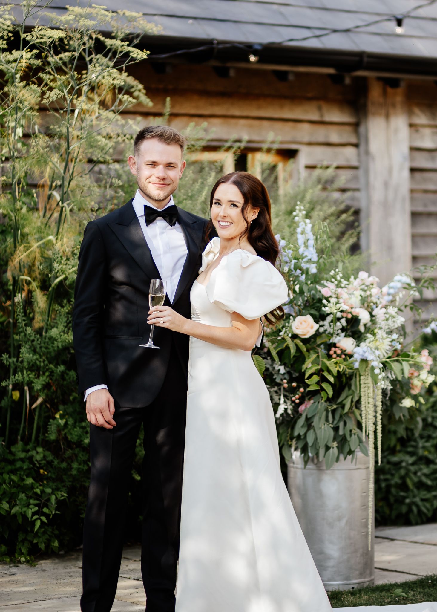 A bride and groom share a romantic moment at a rustic outdoor wedding venue with natural greenery decor.