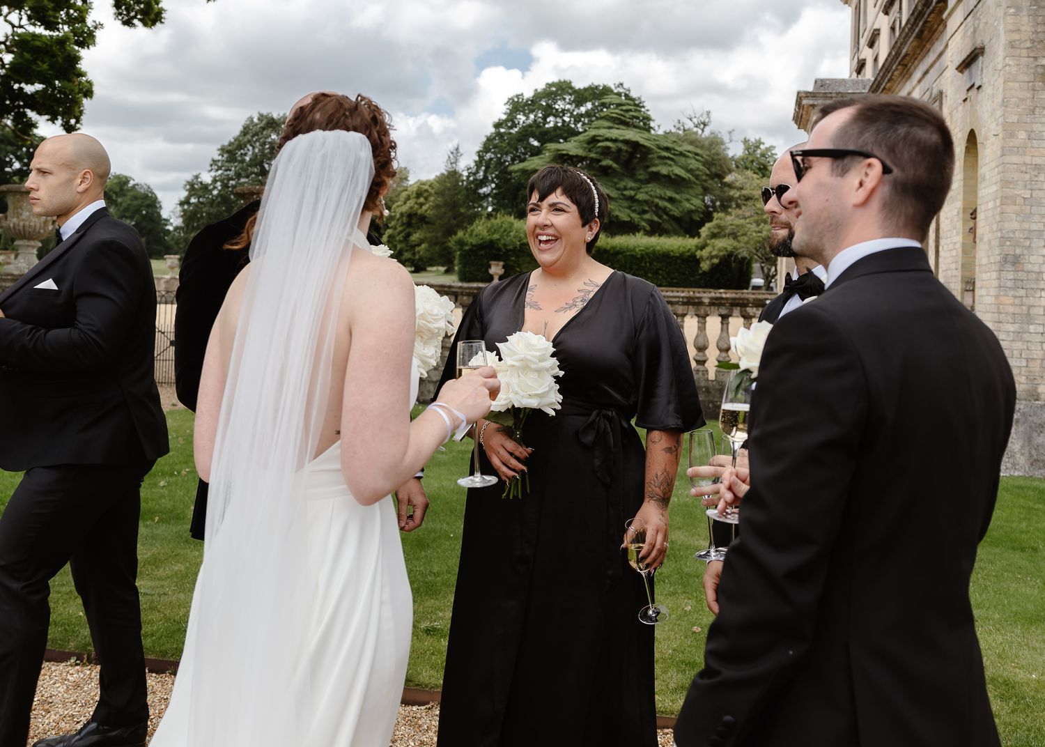 Wedding party members interact during outdoor photo session at elegant estate.