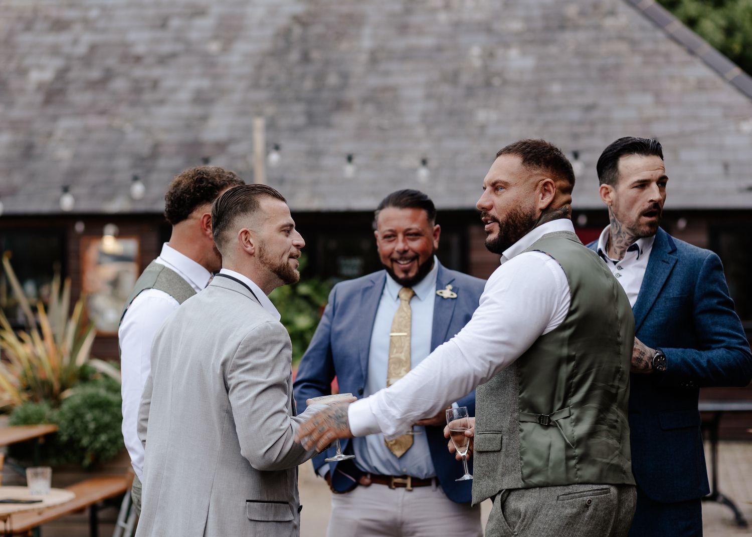Wedding party members in coordinated suits laugh and interact during outdoor photo session.