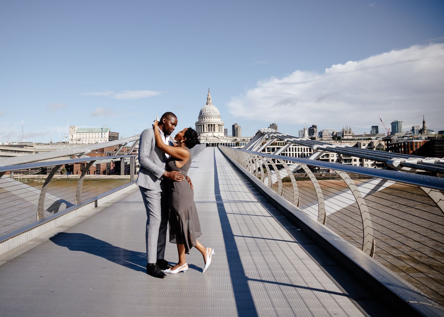 A romantic couple embraces on the Millennium Bridge in London with St Paul's Cathedral in the background.
