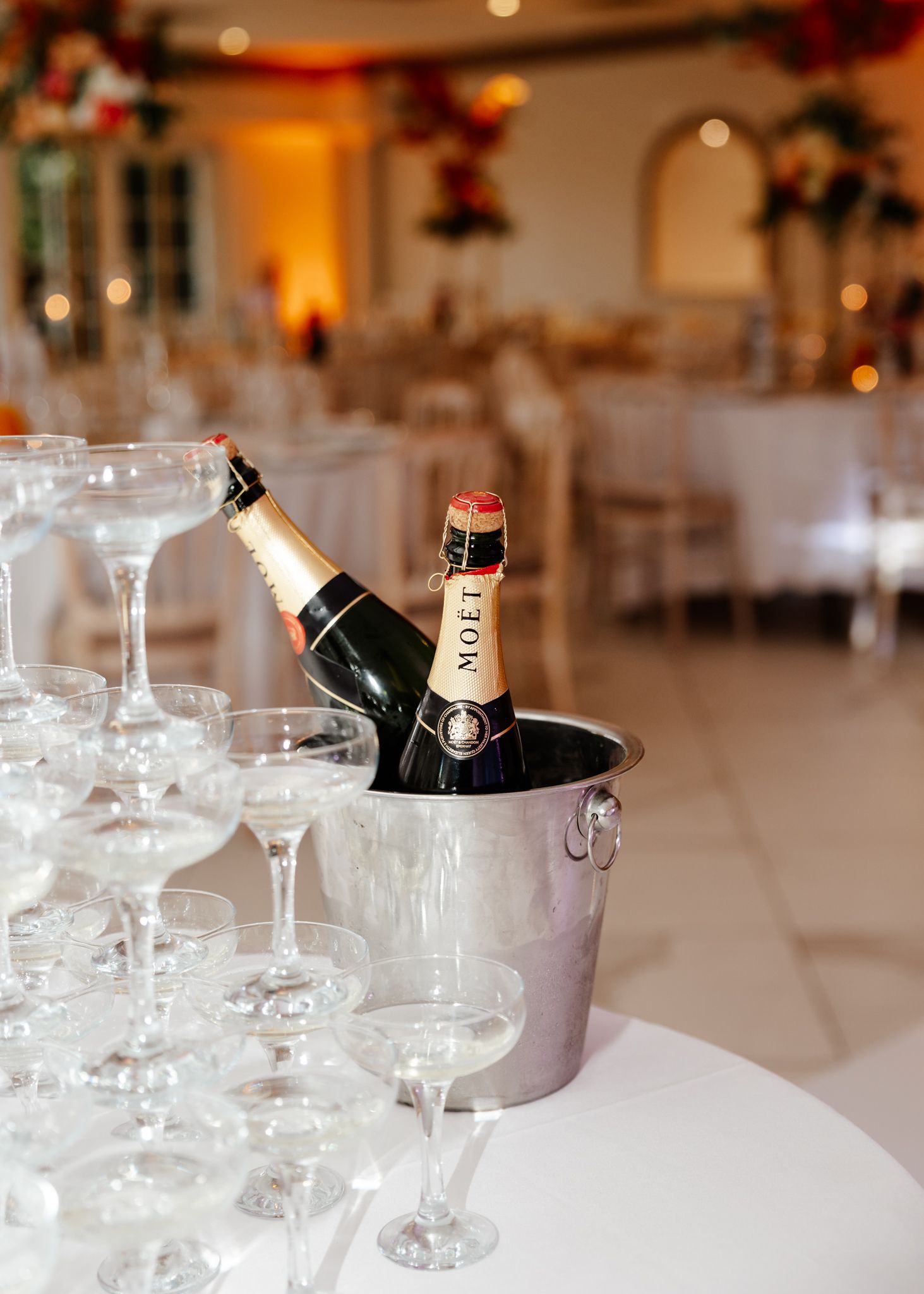 Wine bottles chilling in silver ice buckets on elegant white tablecloth settings at an upscale event venue.