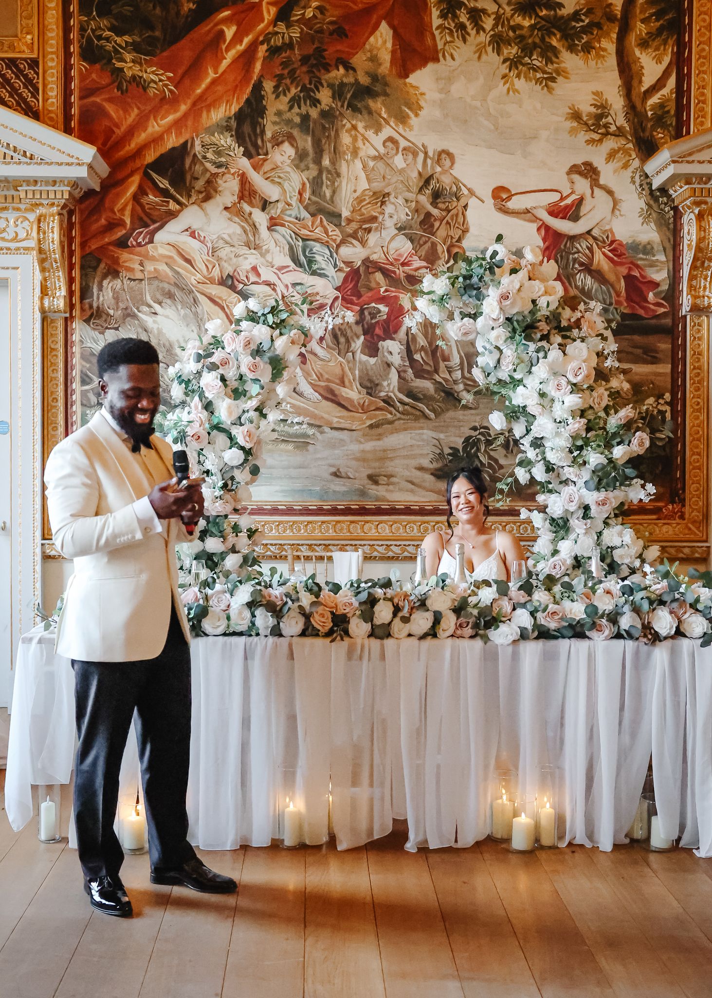 Elegant wedding reception setup in a grand hall with ornate tapestries and floral arrangements along white-draped tables.