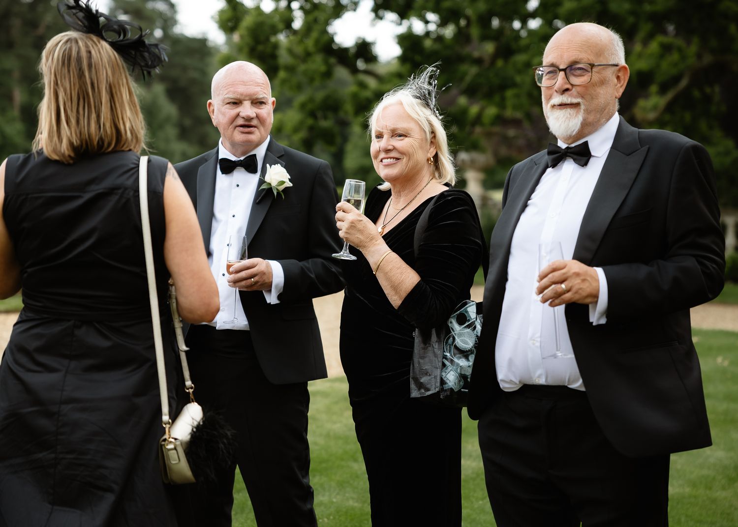 Wedding party in formal black and white attire gathered outdoors for group photos.