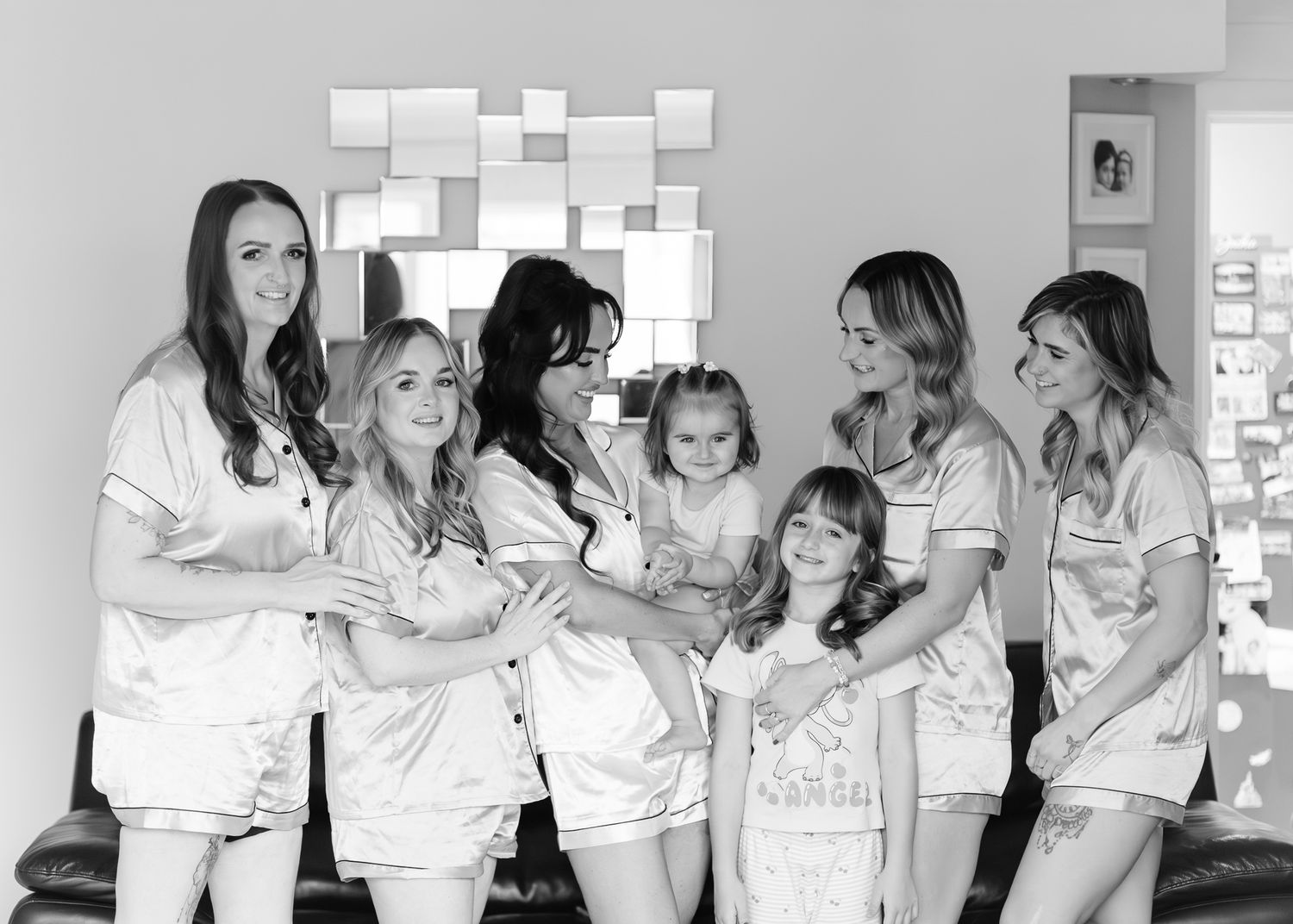 Black and white photo of a group of women and children in matching white robes smiling together in a casual setting.