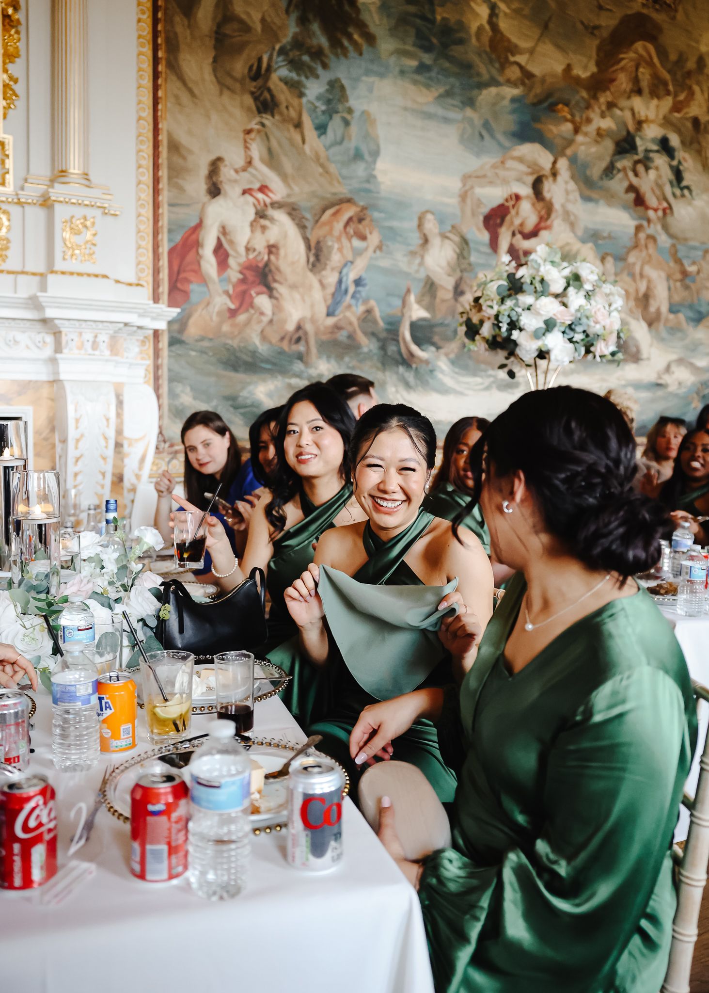 Wedding guests in emerald green dresses celebrate at a reception with ornate ceiling murals and table settings.