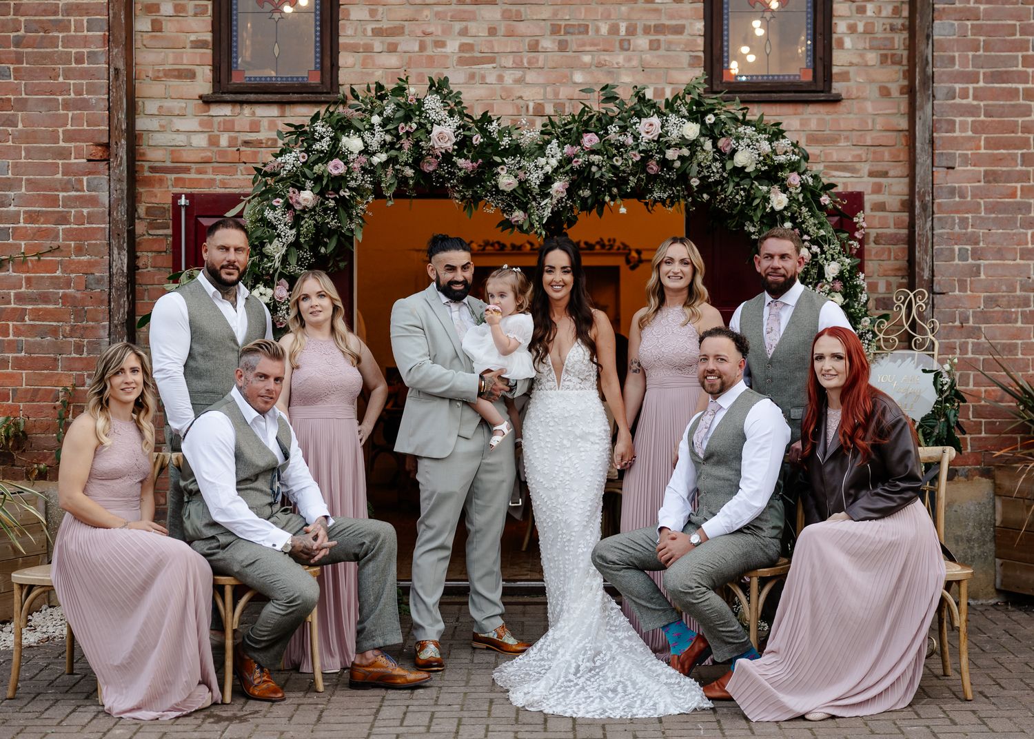 Wedding party poses together on brick patio in blush pink dresses and gray suits.