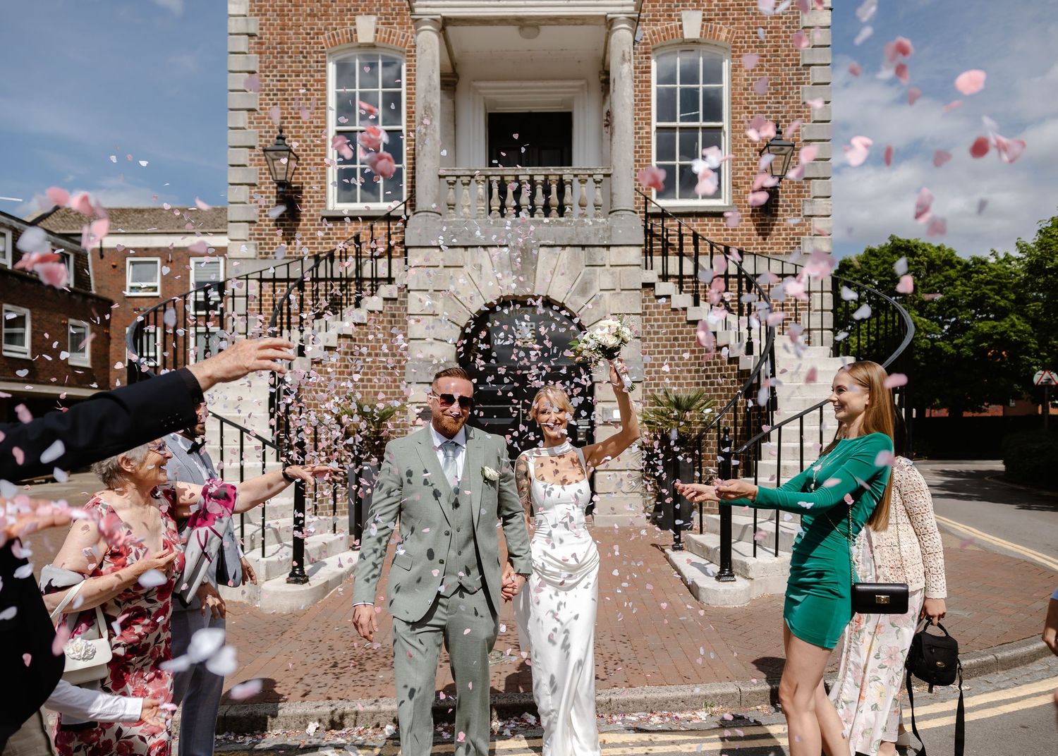 Bride and groom walk through confetti outside a brick building after their wedding ceremony.