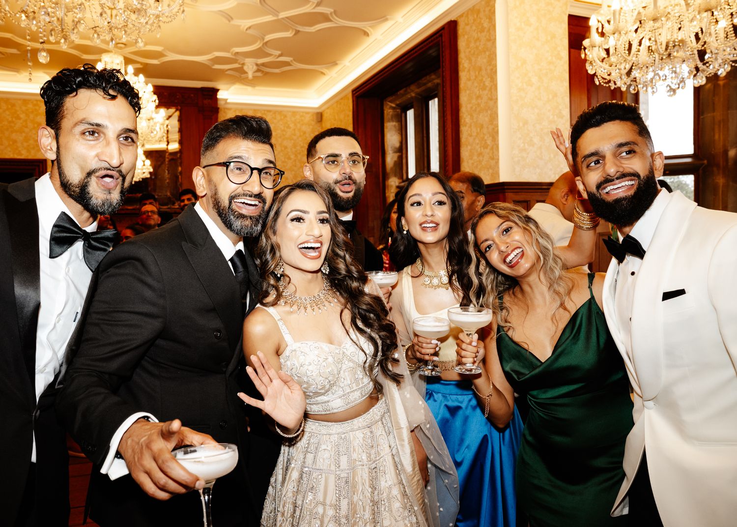 Wedding guests dance and celebrate together on a dance floor at an elegant reception venue with warm lighting.